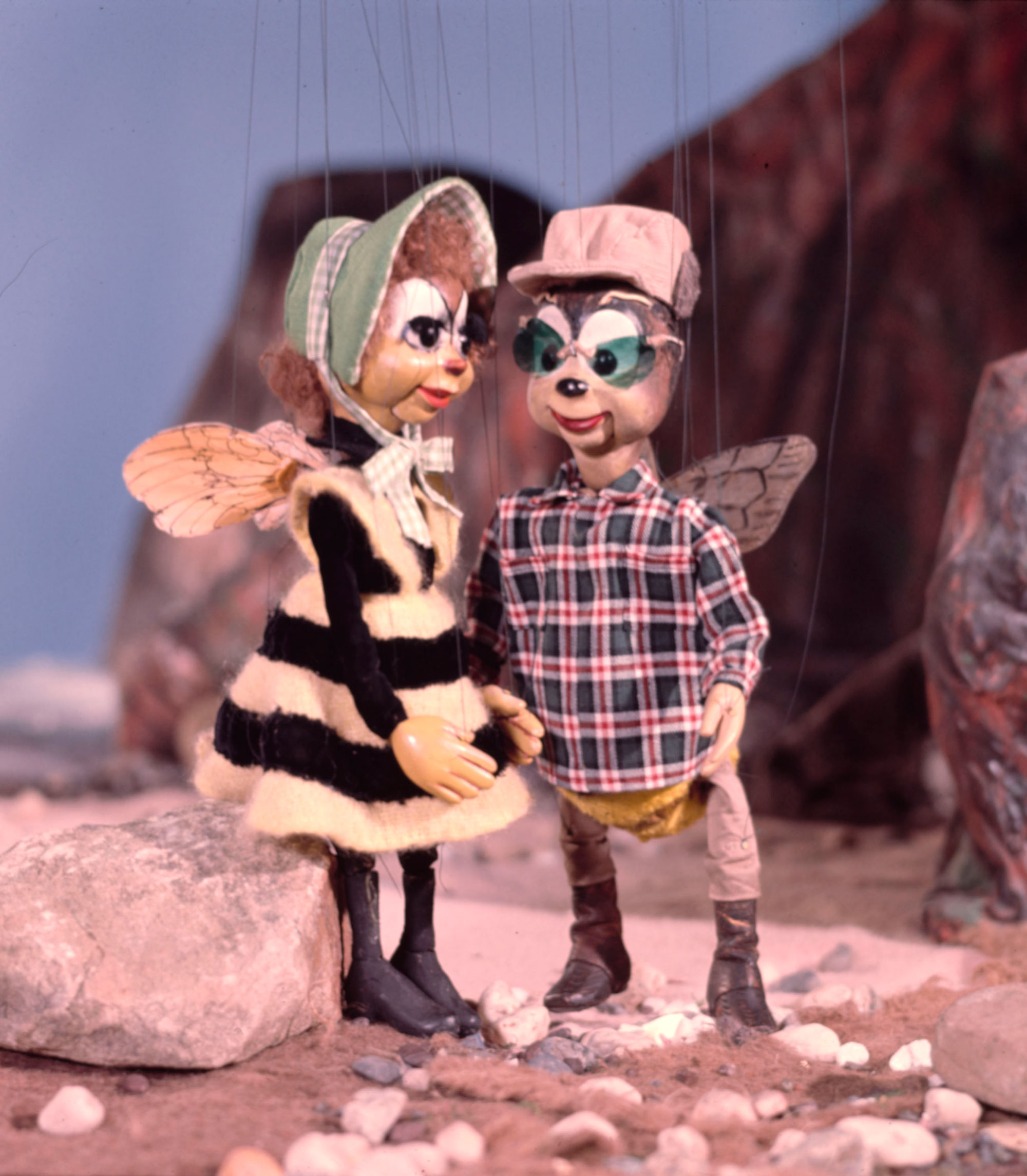 Two bee puppets dressed in clothes on a rocky set