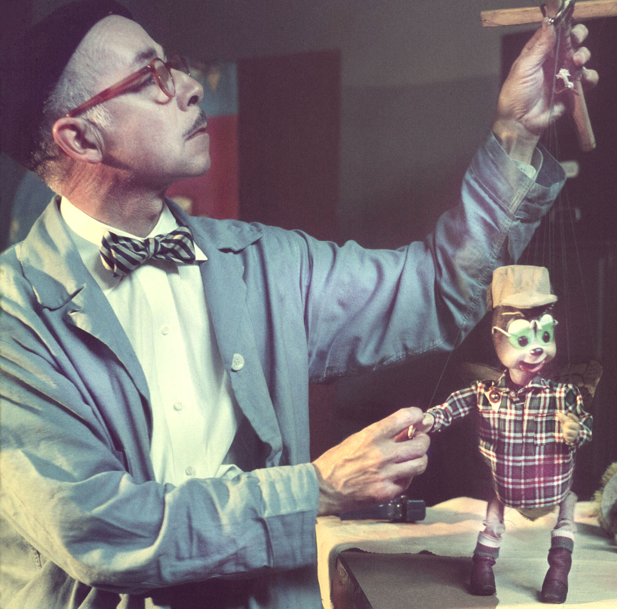 Man in glasses and bowtie holds puppet controls above small bee puppet