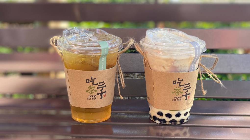 Two boba drinks on a park bench.