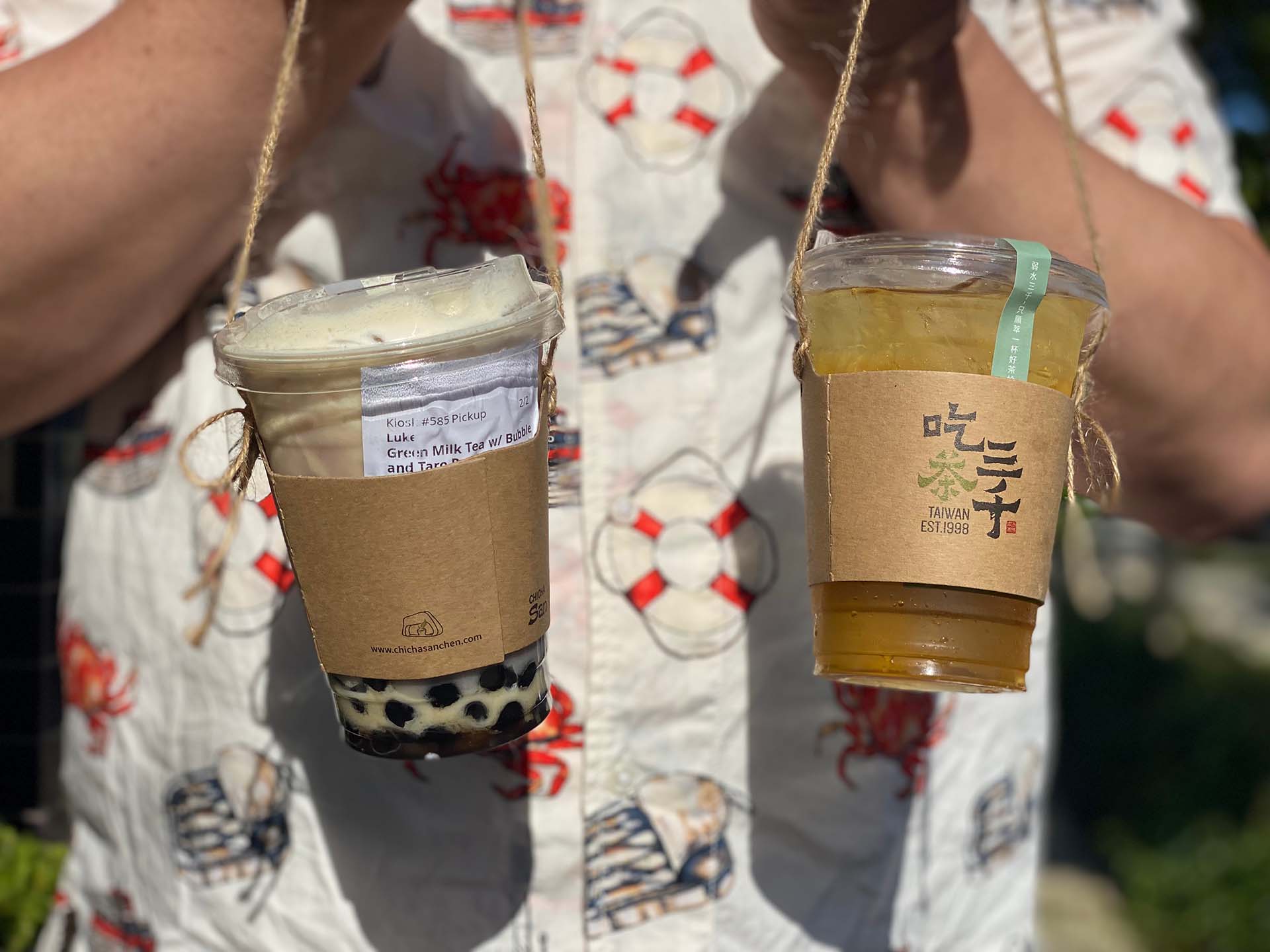 Close-up of a man holding two boba drinks using boba totes made of twine.