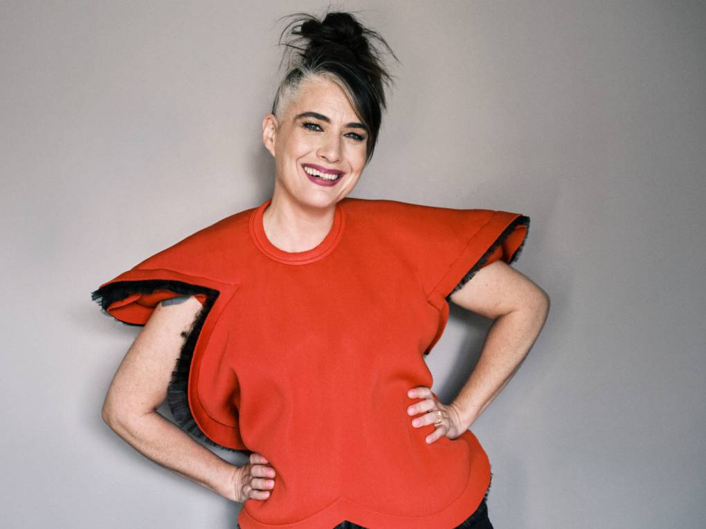A smiling middle aged women stands with her hands on her hips in an oversized, structured top.