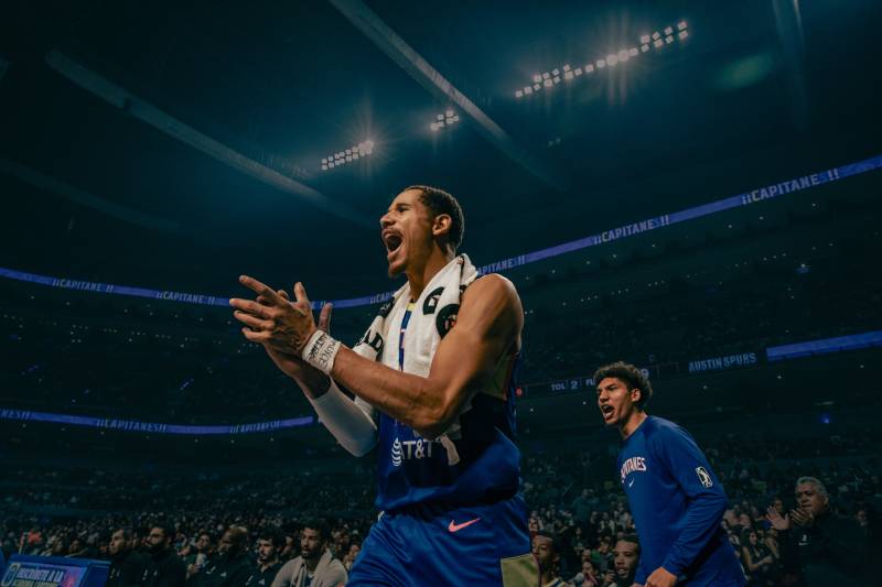 a basketball player cheers on his teammates from the sideline inside an arena