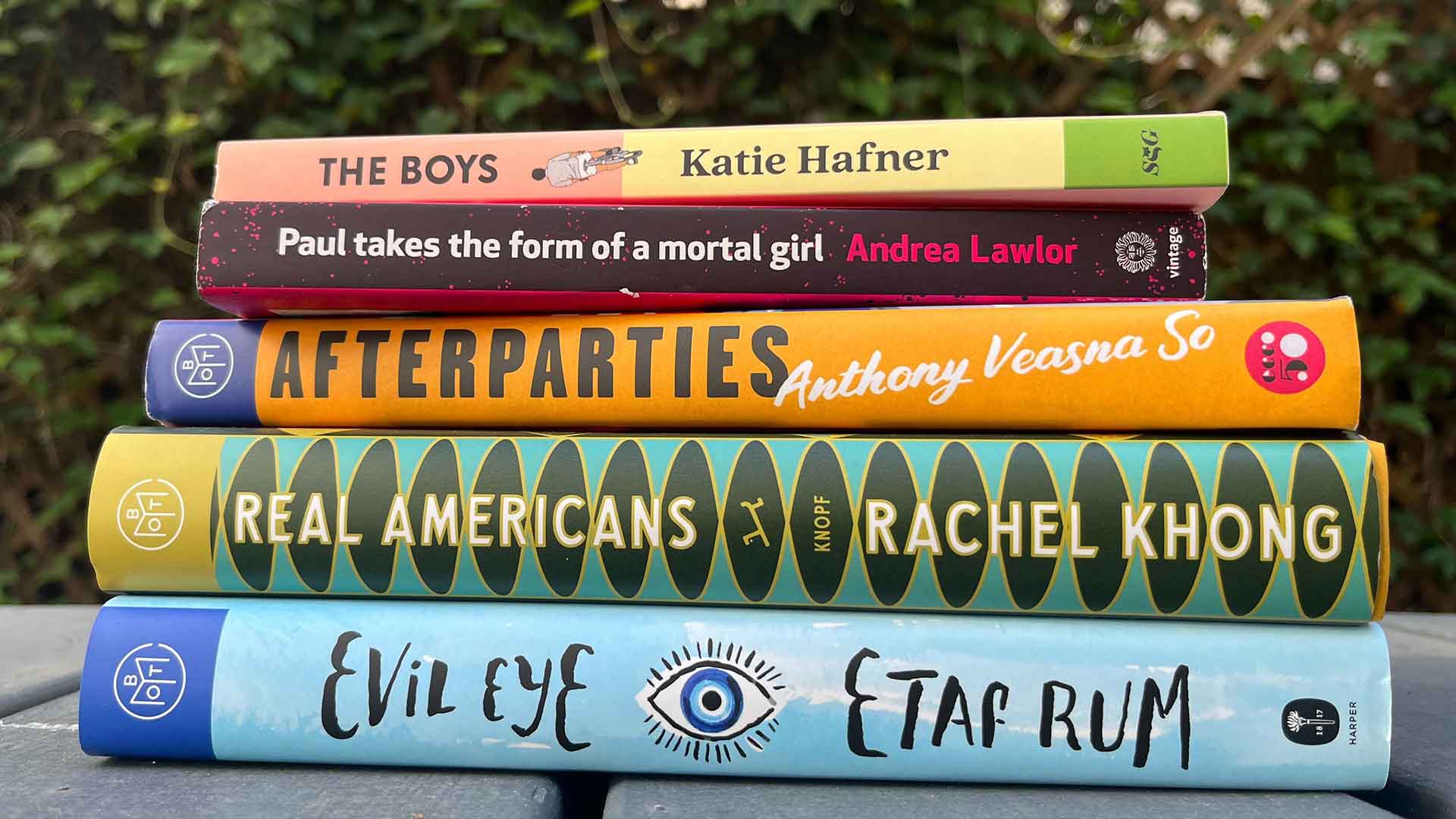 A pile of books, with spines showing, against a backdrop of ivy.