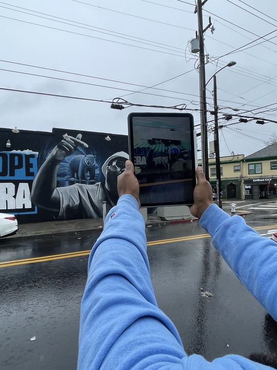 Damien McDuffie shows how his augmented reality app works on a mural of Oakland's Mistah F.A.B.
