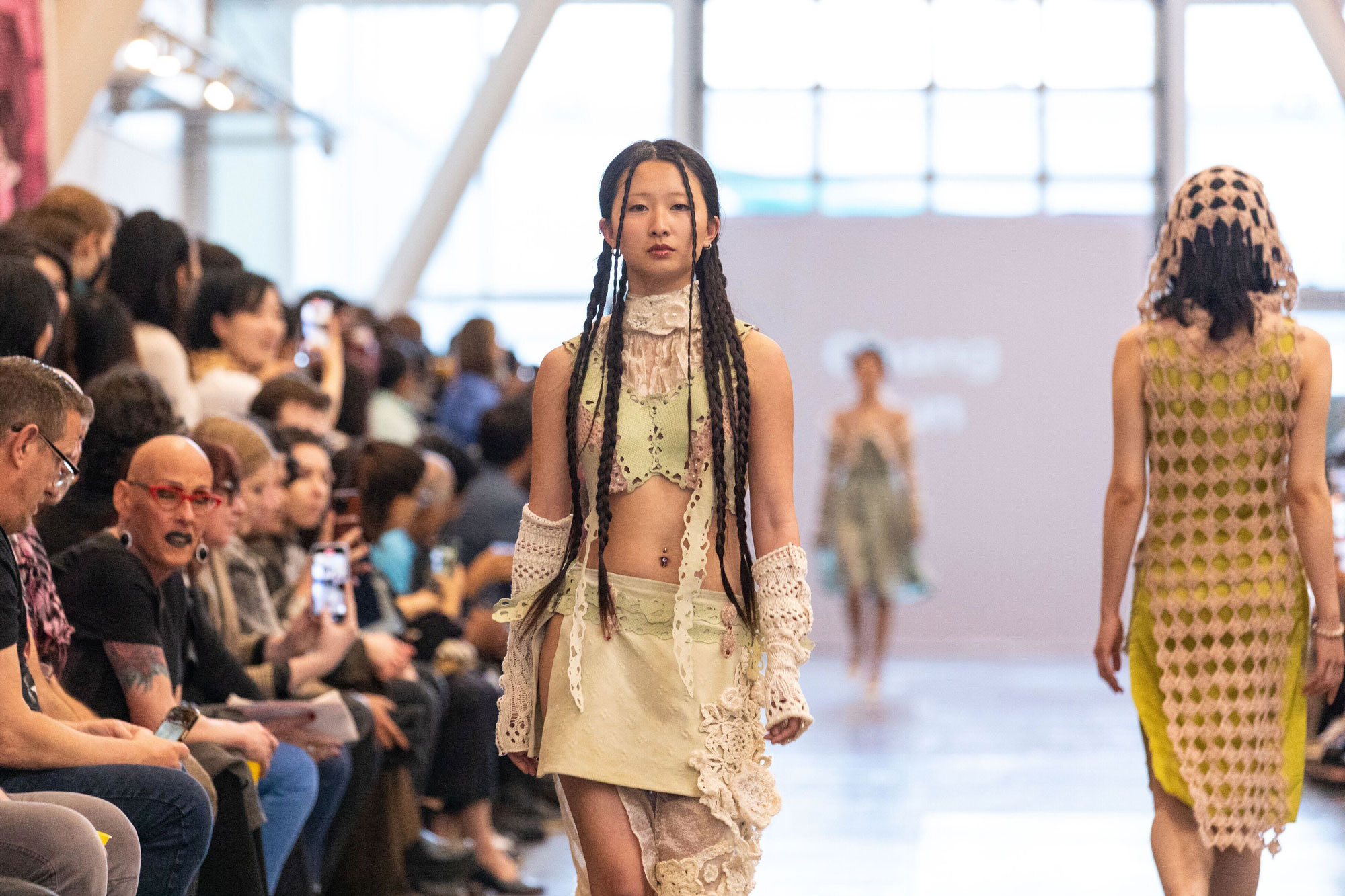Two models on runway with crowd watching at left