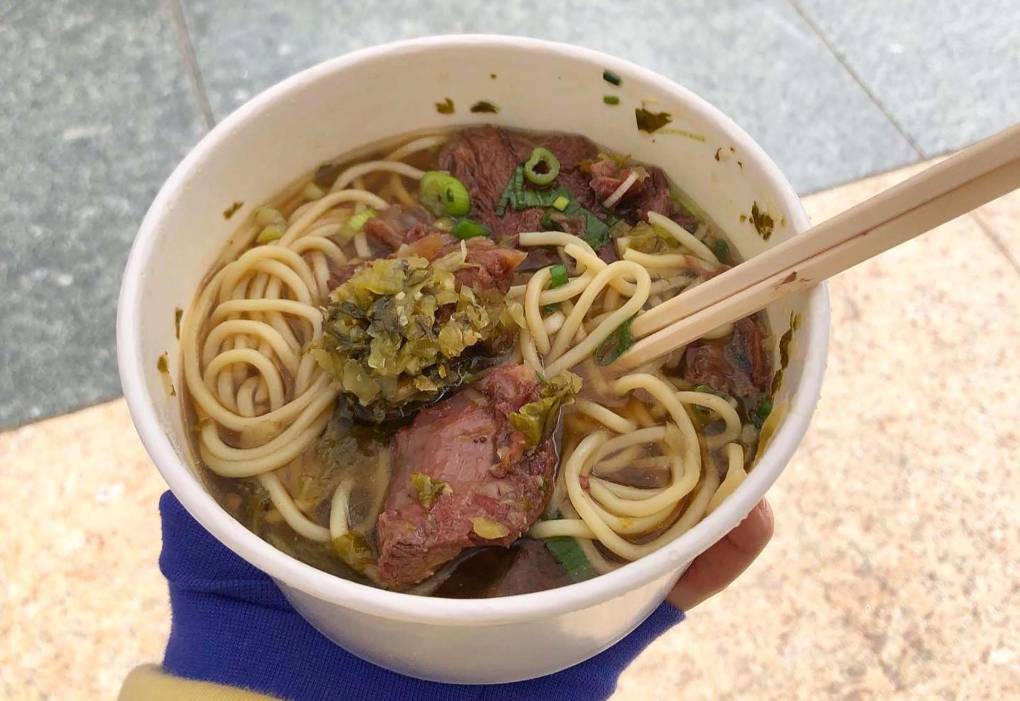 Beef noodle soup in a takeout bowl.