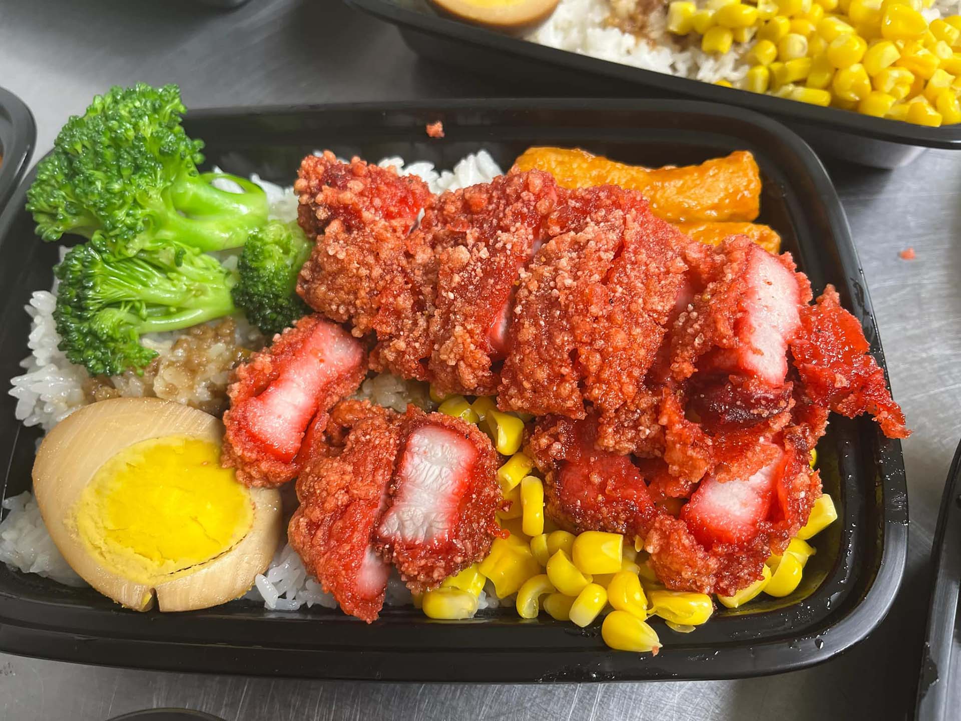 A red pork chop bento wit corn and egg.