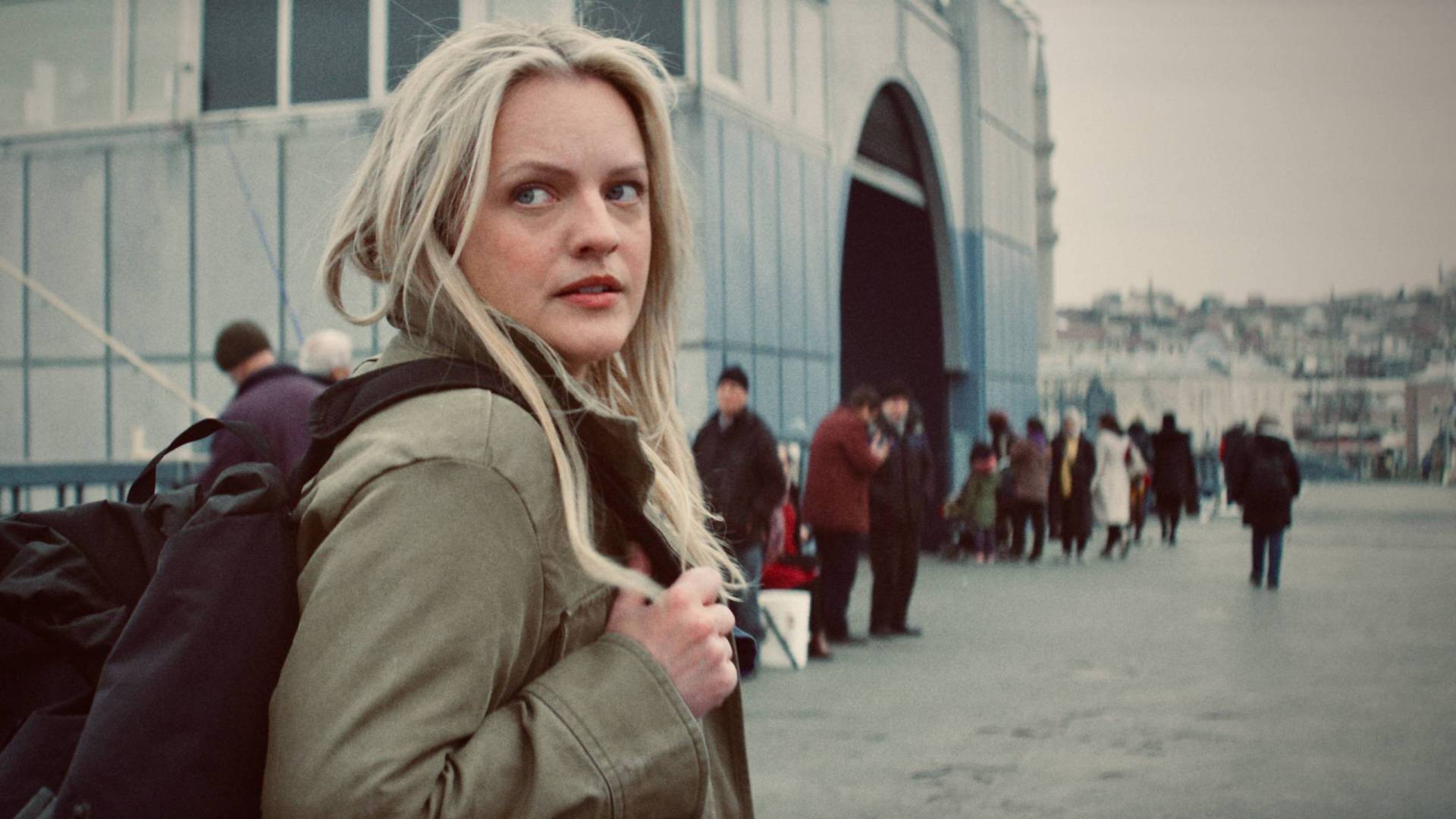 A white woman with long blonde hair approaches a busy depot, peering over her shoulder suspiciously.