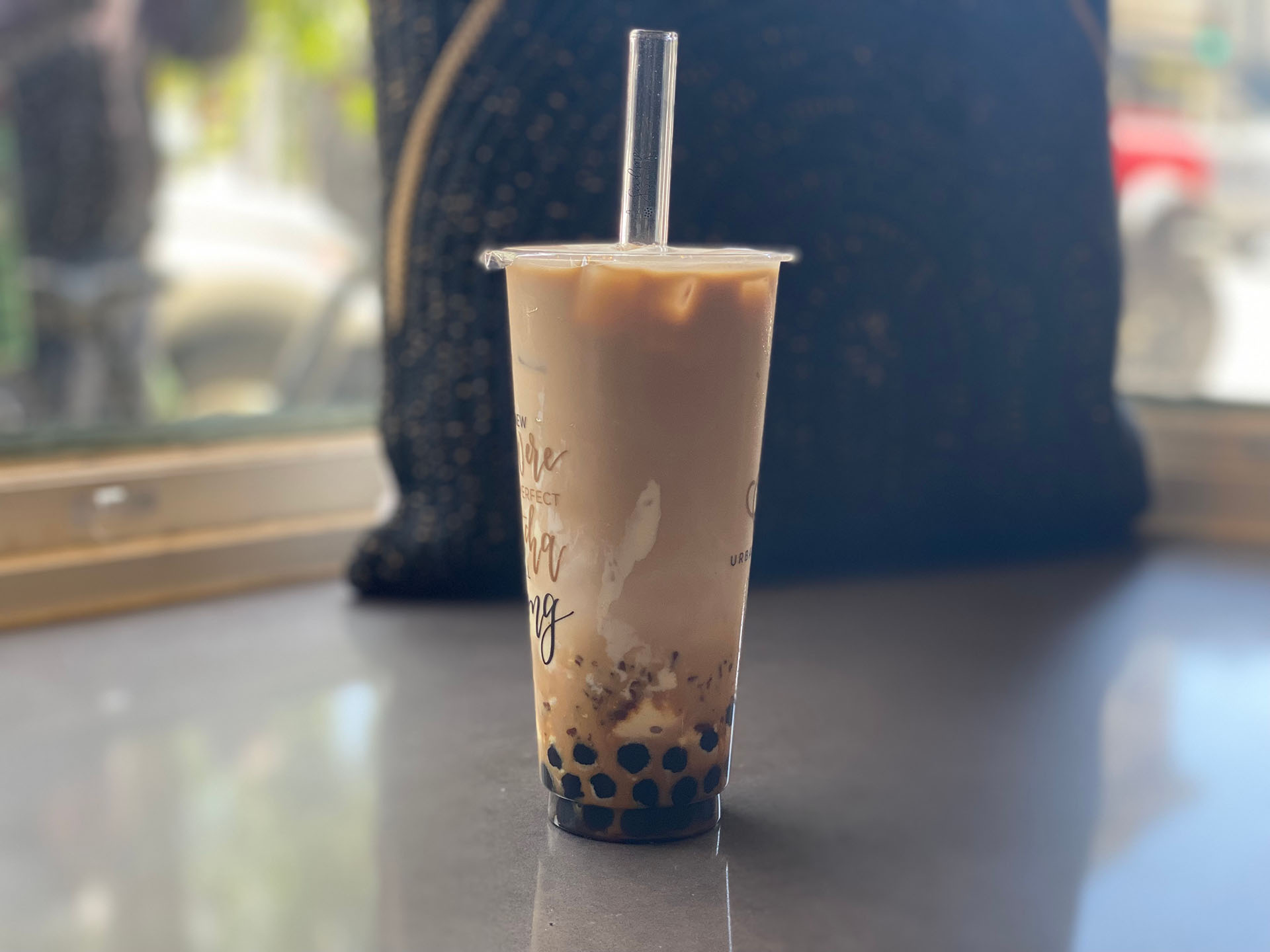 A creamy boba drink sits on a table in front of a pillow.