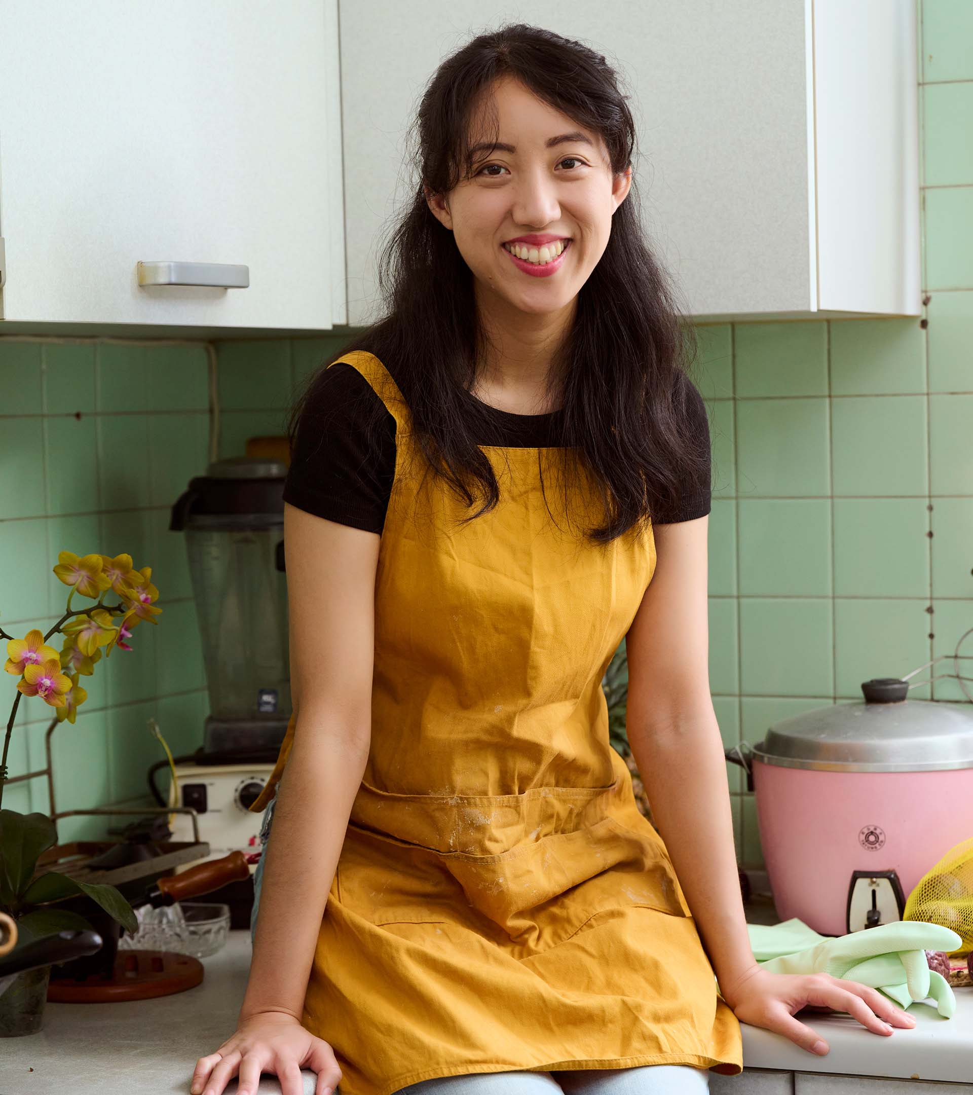 Headshot portrait of food writer Clarissa Wei, in her kitchen wearing a yellow apron.