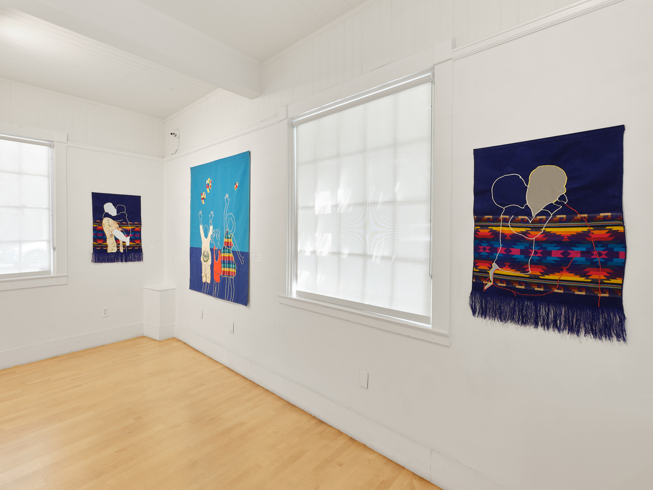 three textile pieces on white walls with windows