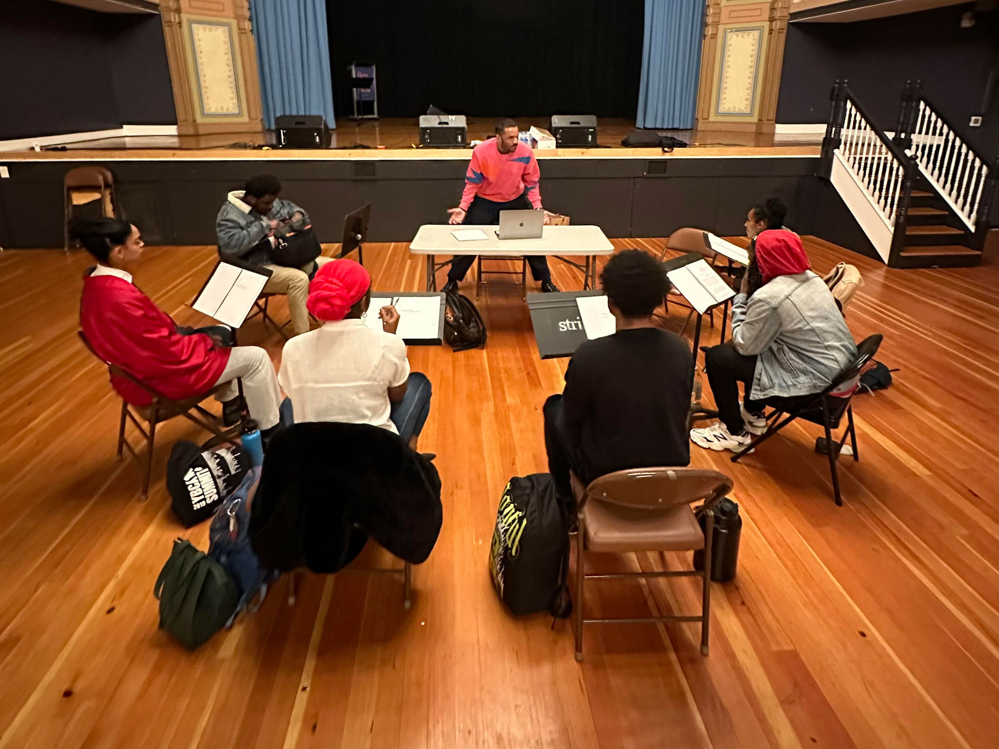 One man standing at table in circle of seated people in theater space