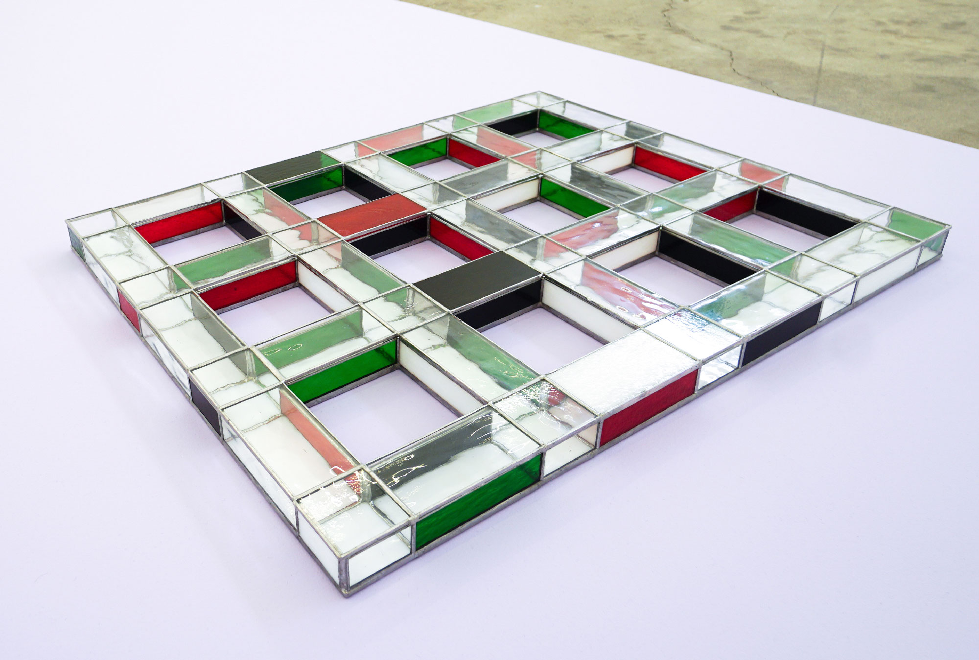 Red, green, white and clear stained-glass grid sculpture on lavender platform