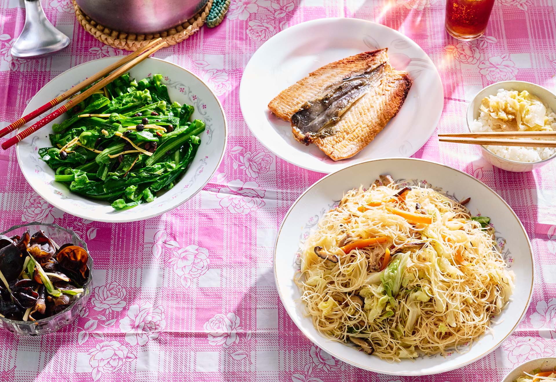 A spread of homestyle Taiwanese dishes laid out on a pink and white checked tablecloth.