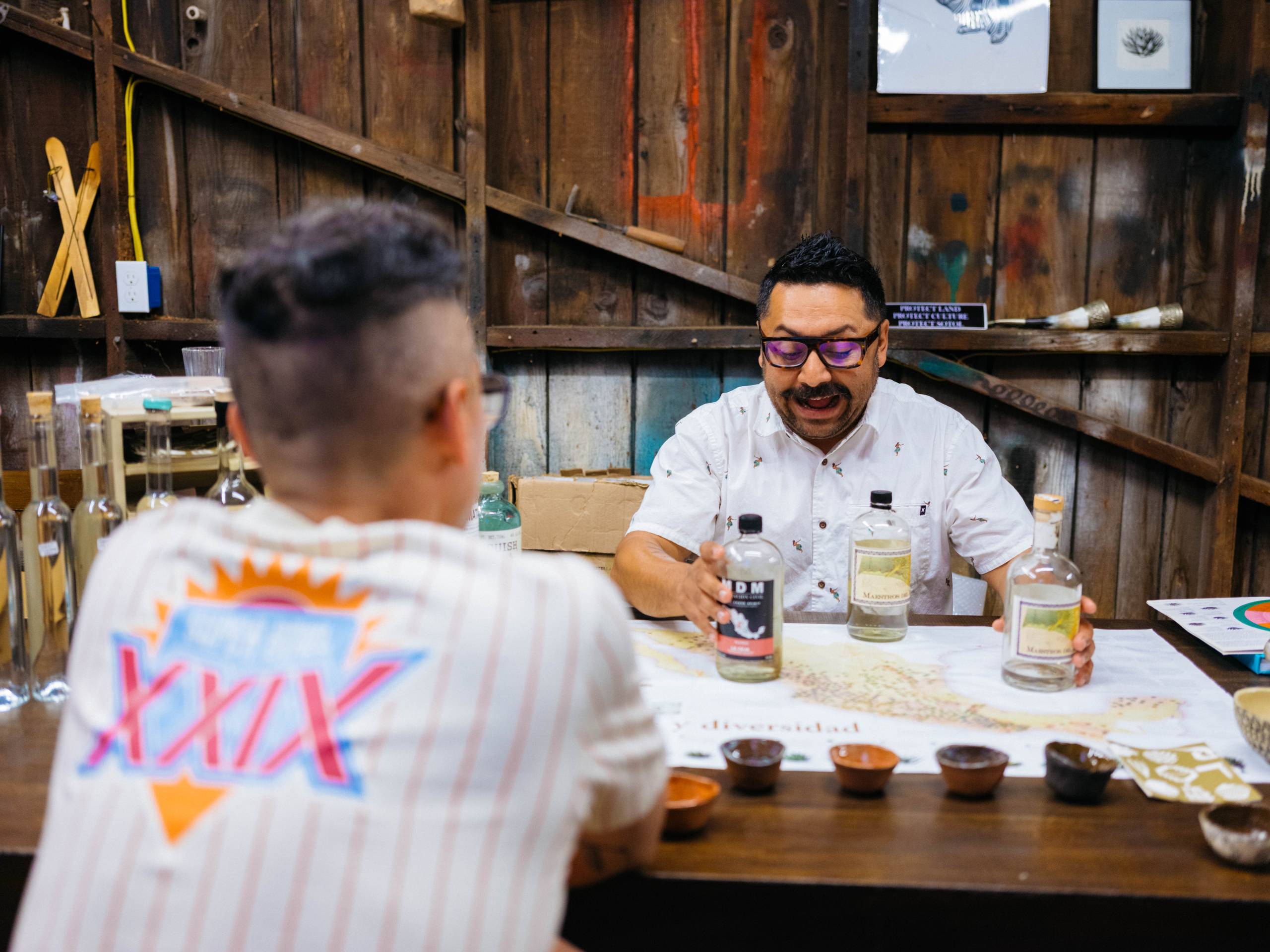 a mezcal expert explains his favorite mezcal options to a journalist sitting at the same table
