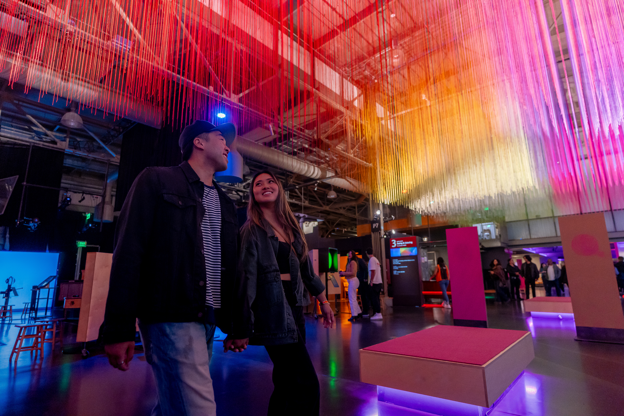 People walk under hanging strings in rainbow colors