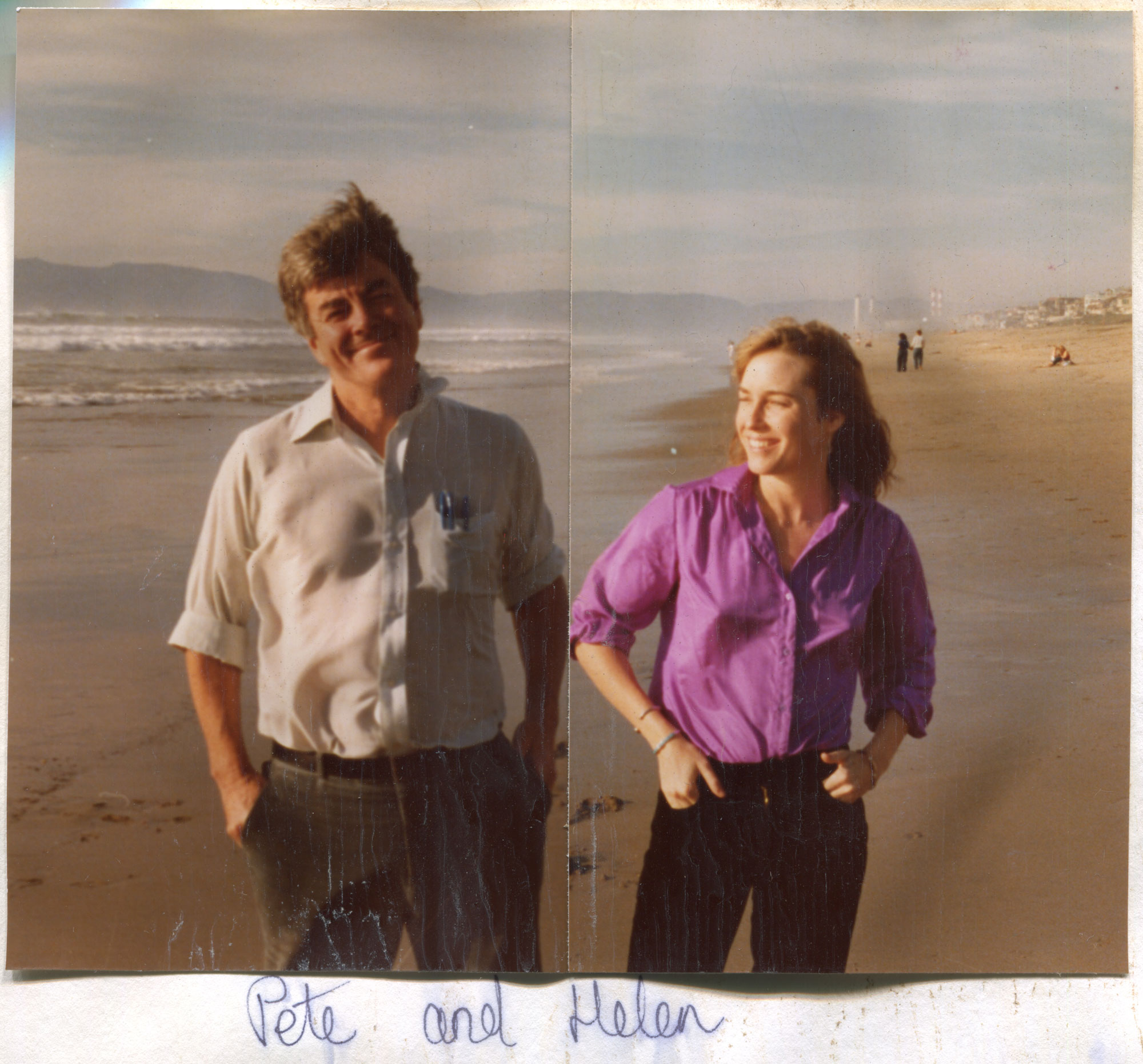 Man and woman stand smiling on beach with names written below photograph