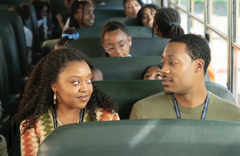 A Black woman and Black man sit together at the front of a school bus.