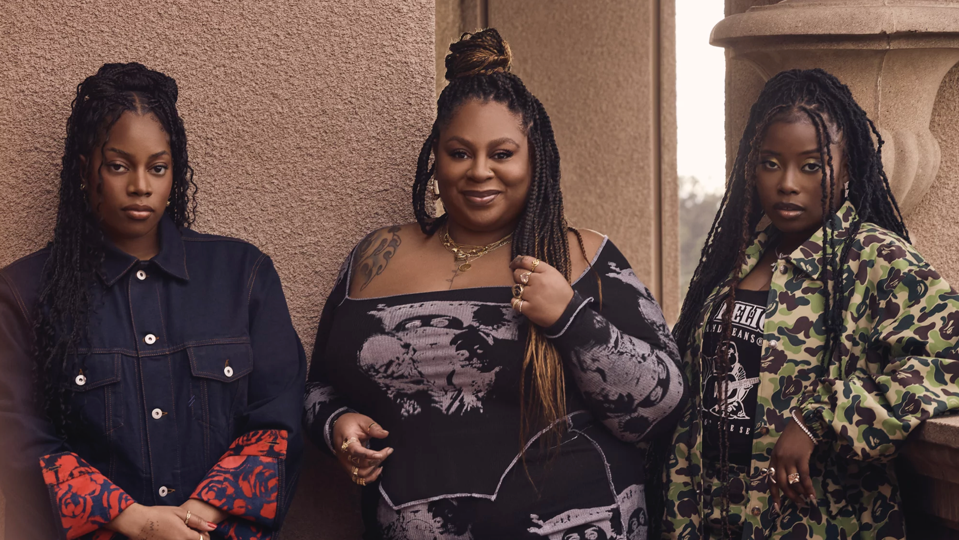 Three Black women stand side by side wearing cool clothes.