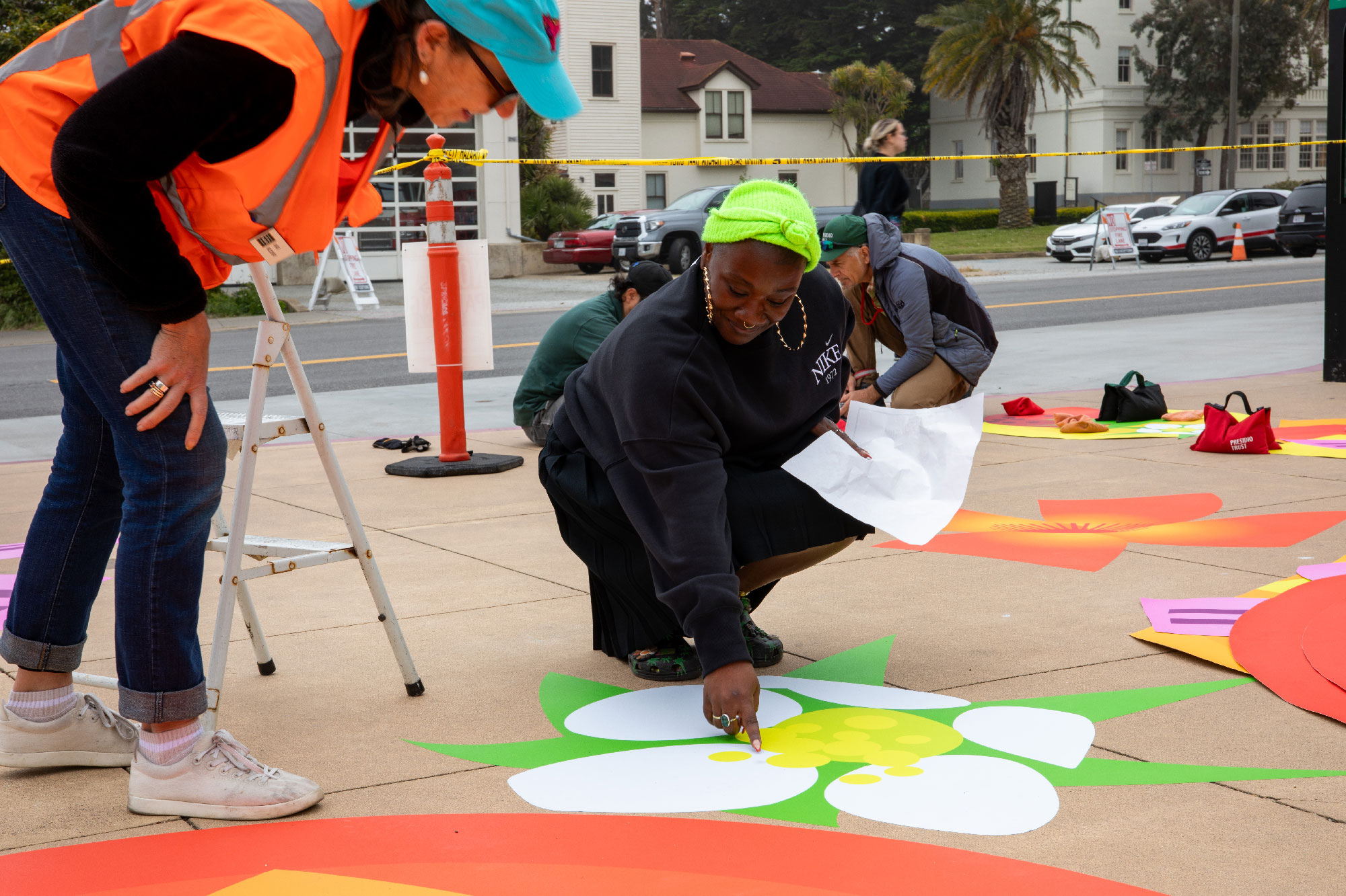 person in safety vests leans over as another person points to large decal on sidewalk