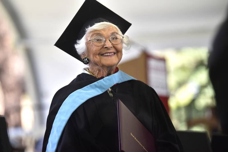 A senior woman smiles broadly while wearing a cap and gown.