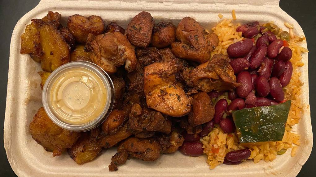 Chunks of fried chicken with red beans and yellow rice in a takeout carton.