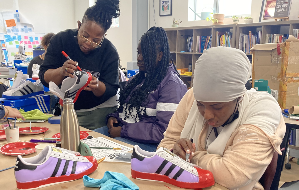 a group of young women customize Adidas sneakers with paint