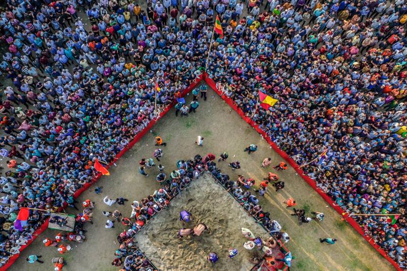 A large crowd gathers around a designated space where two wrestlers are engaged in a match.