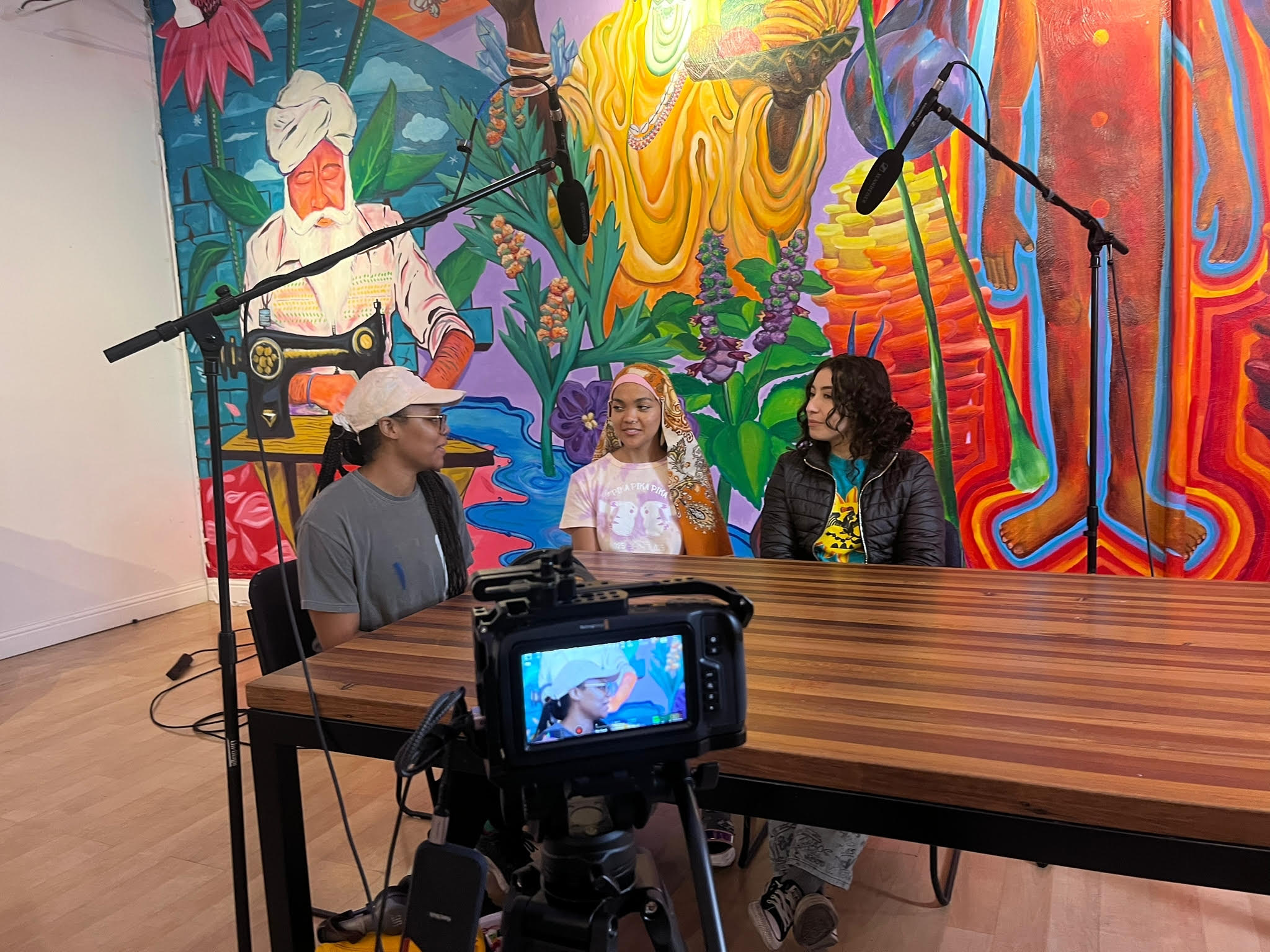 Three artists sit at a table during the filming of a documentary.
