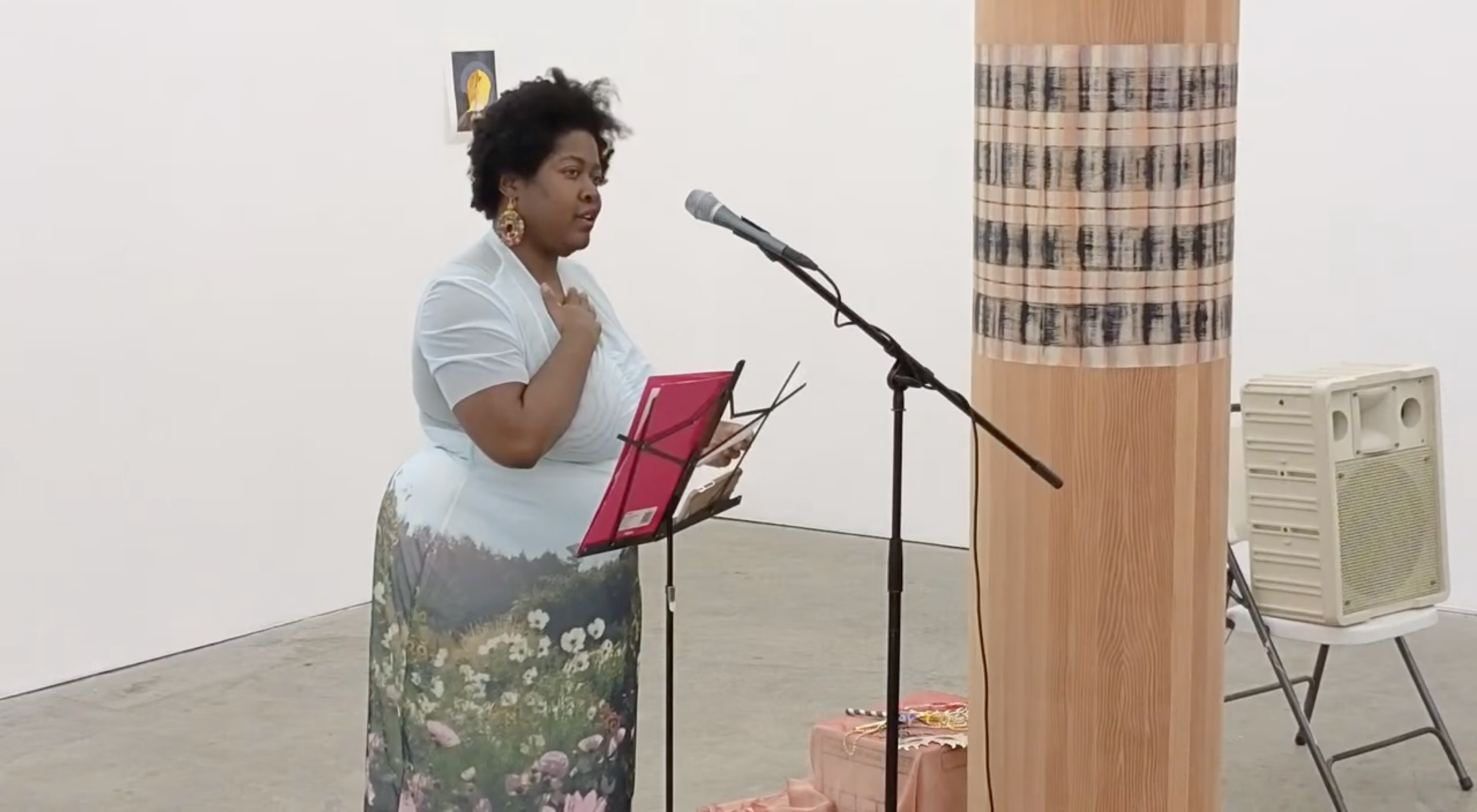 Black woman stands with right hand on chest in front of mic in gallery space