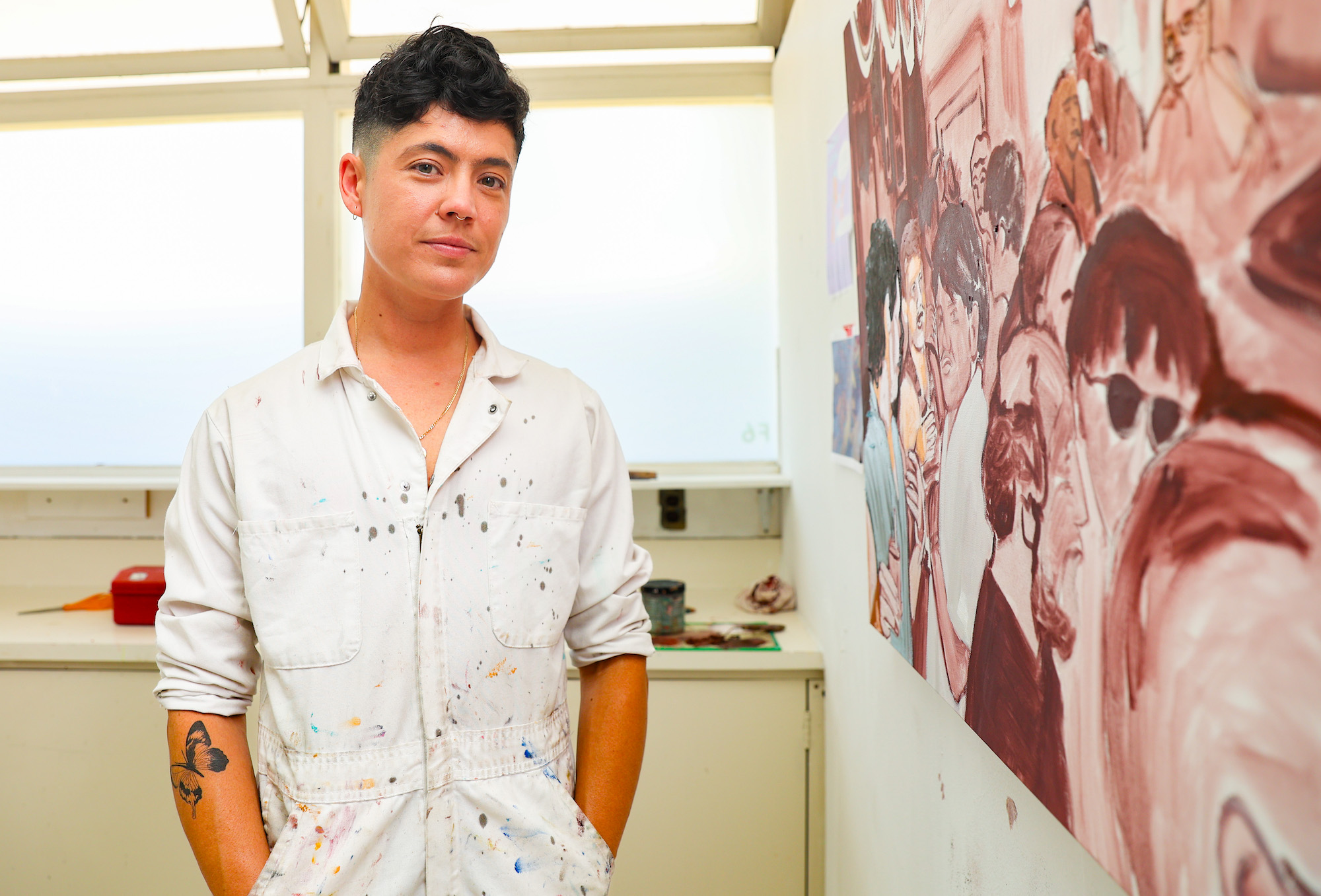 person with short hair stands in a painting studio in white jumpsuit