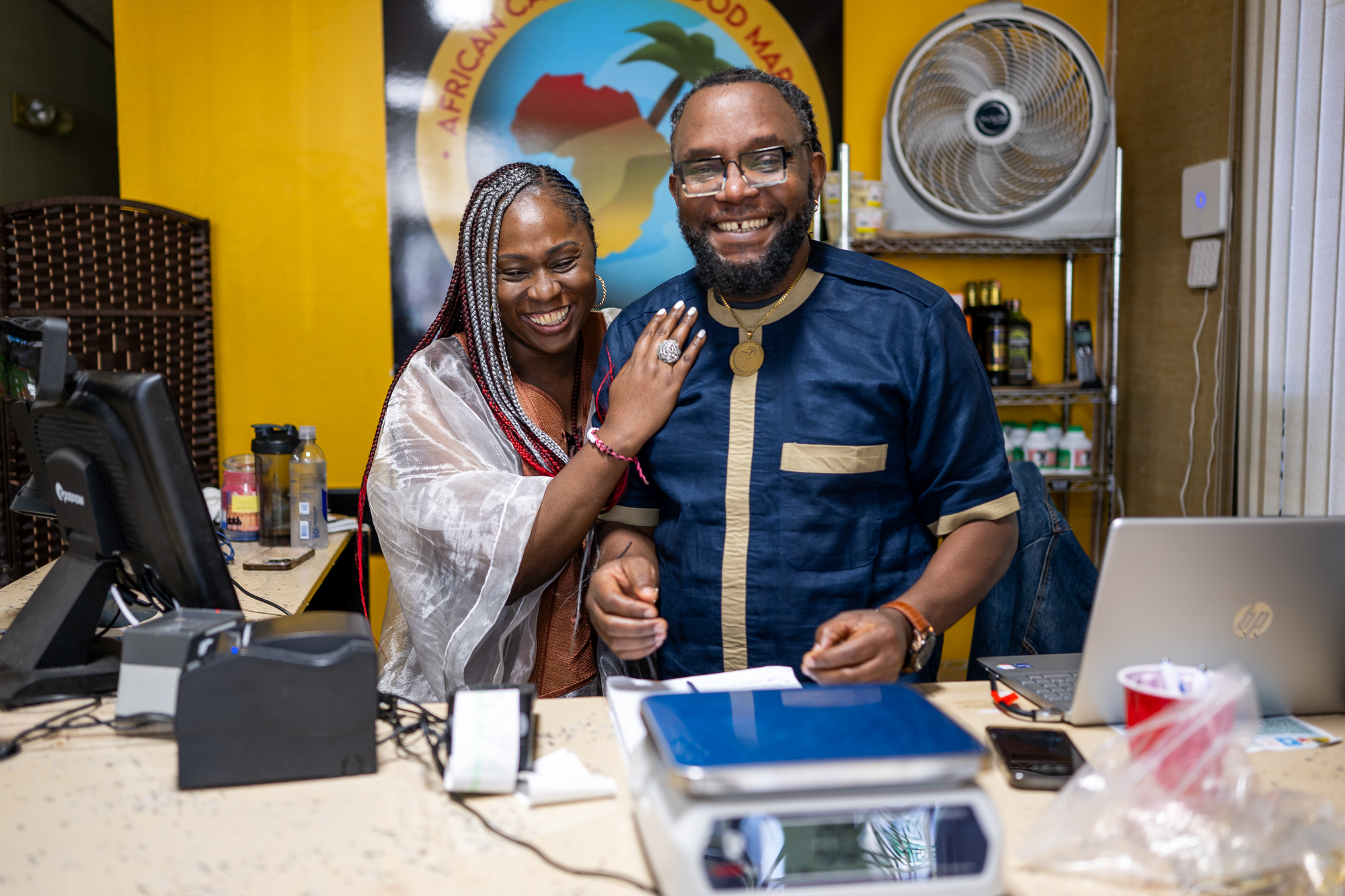 A married couple shares a laugh while standing behind the counter inside the market they run.