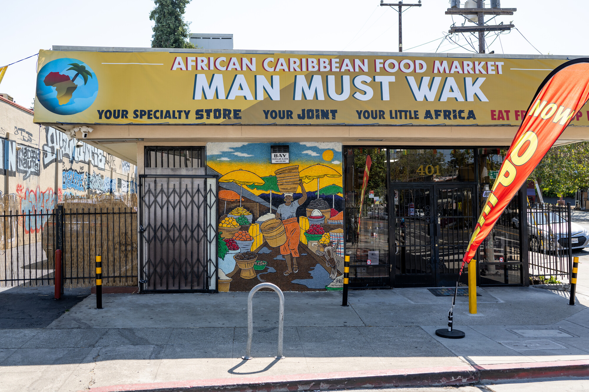 Afro-Caribbean market Man Must Wak's bright yellow storefront with a mural depicting a woman strolling through a bustling African outdoor market.
