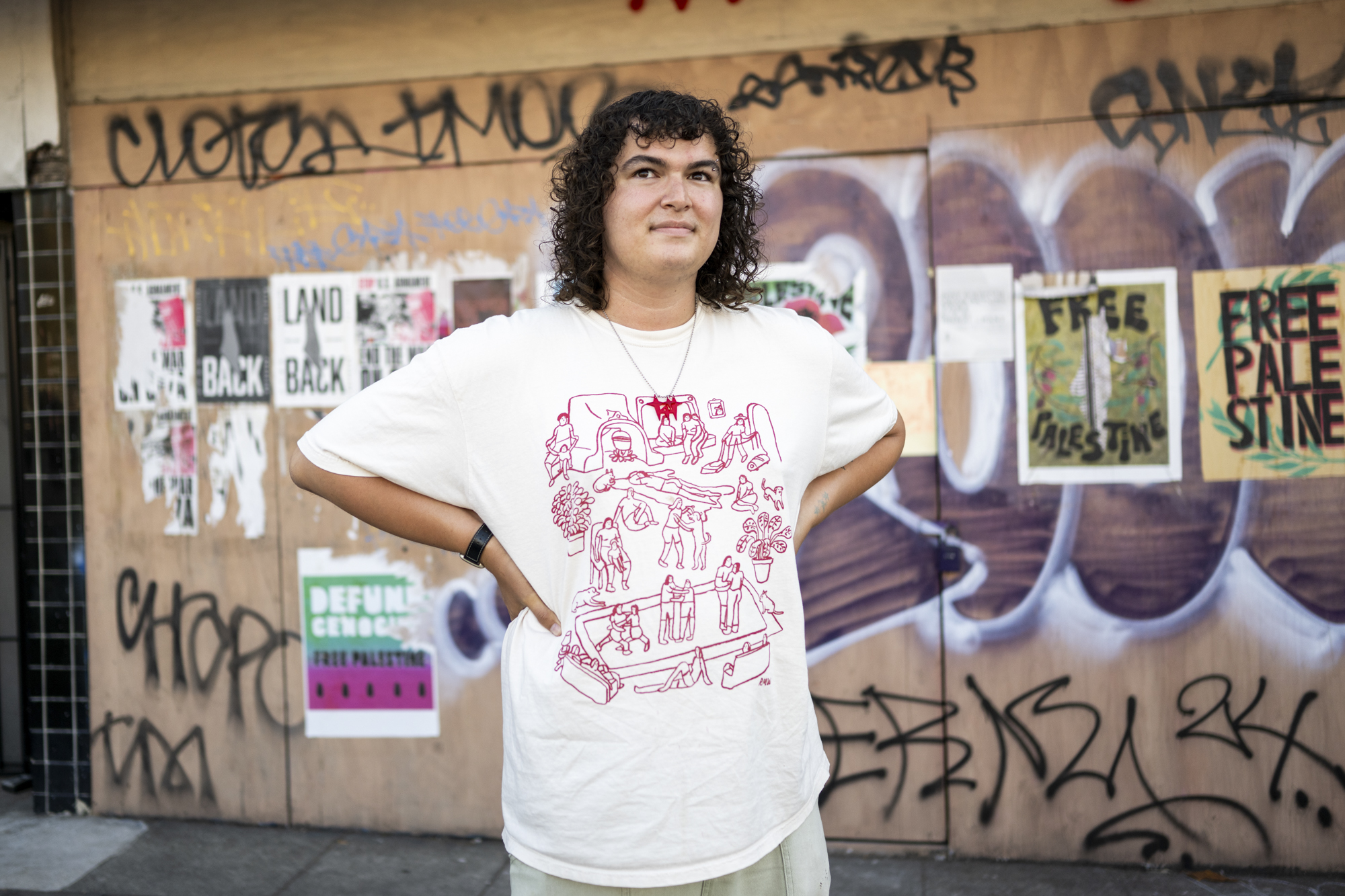 Person stands with hands on hips in front of graffitied storefront
