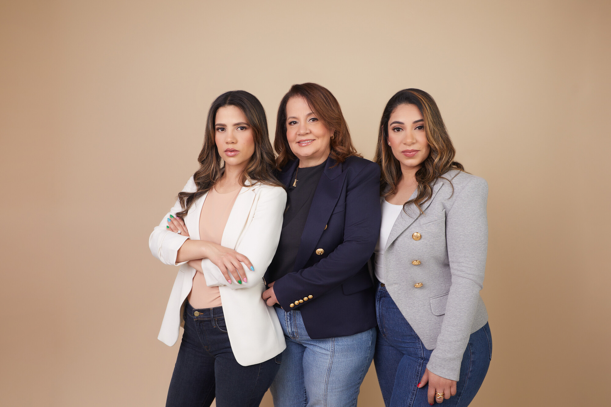 Portrait of a woman (center) and her two adult daughters, all posing in jeans and blazers.
