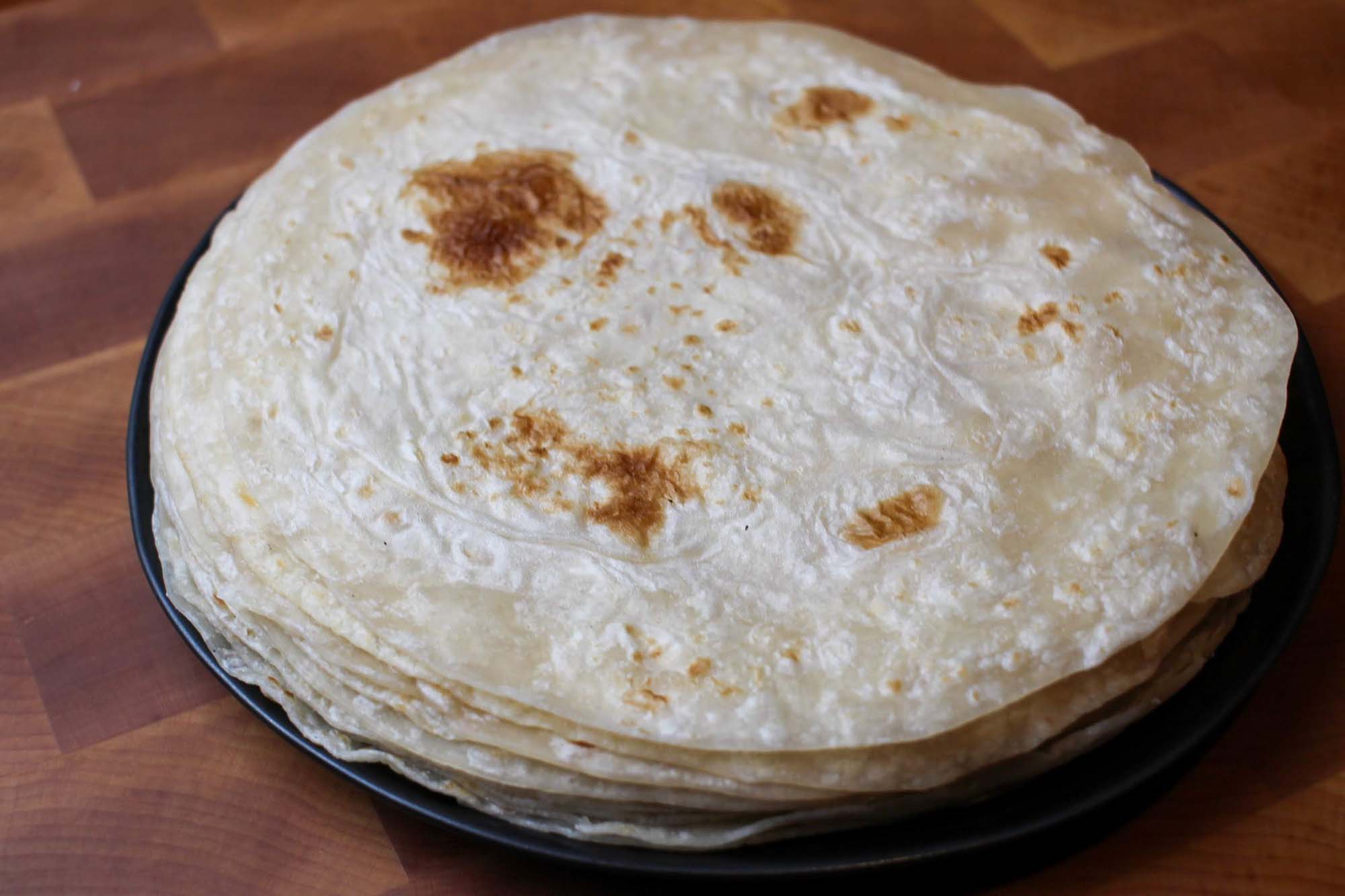 A stack of flour tortillas, blistered in spots.