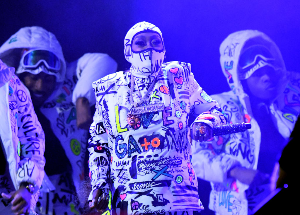 Missy Elliott performs wearing a graffiti-printed bodysuit and balaclava, surrounded by dancers. 