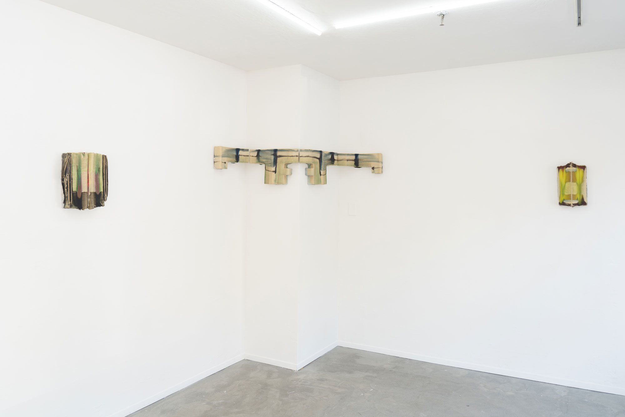 White gallery walls with three abstract ceramic sculptures hanging, one that wraps around a protruding corner