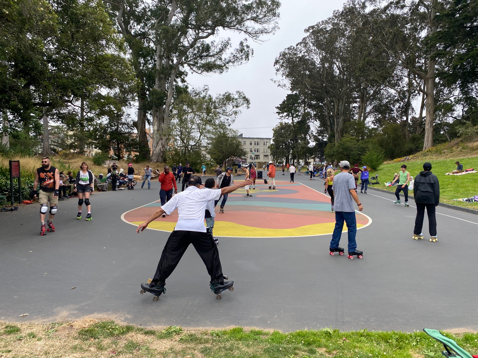 Roller skaters practice in the paved area of a tree-lined park. 