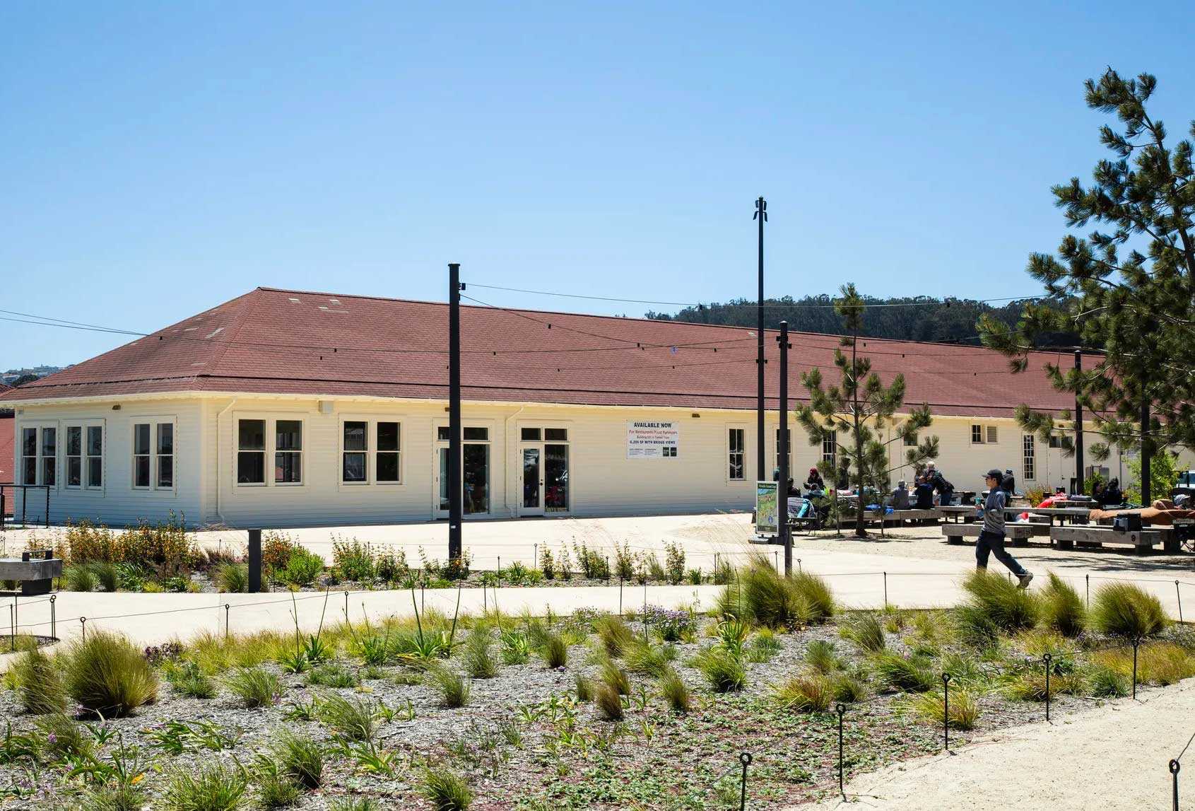 A low-slung white building with composite shingle roof stands against a light blue sky.