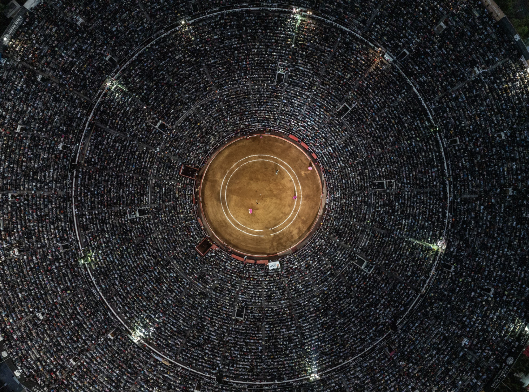 An aerial image of a vast crowd seated in concentric circles around a central ring.