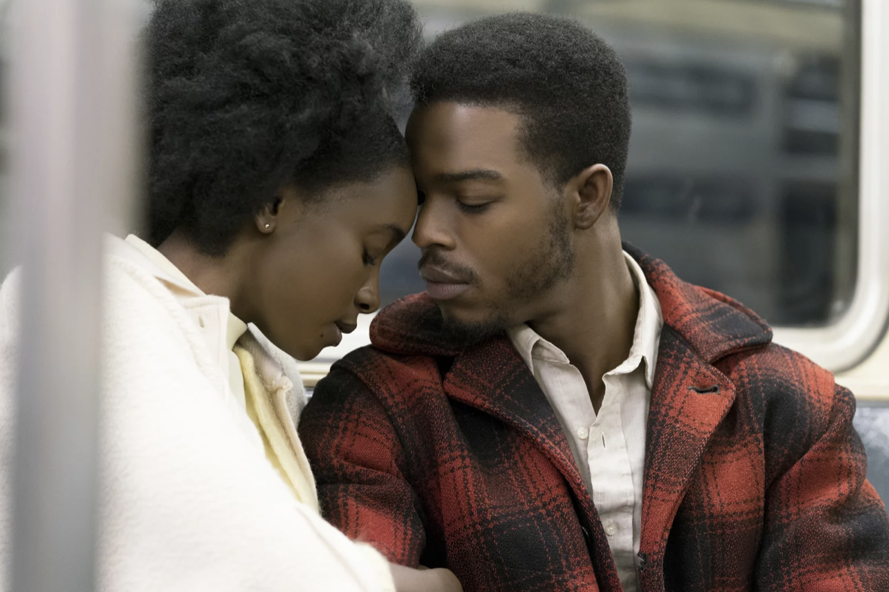 A young Black woman and young Black man sit close together, their foreheads touching.