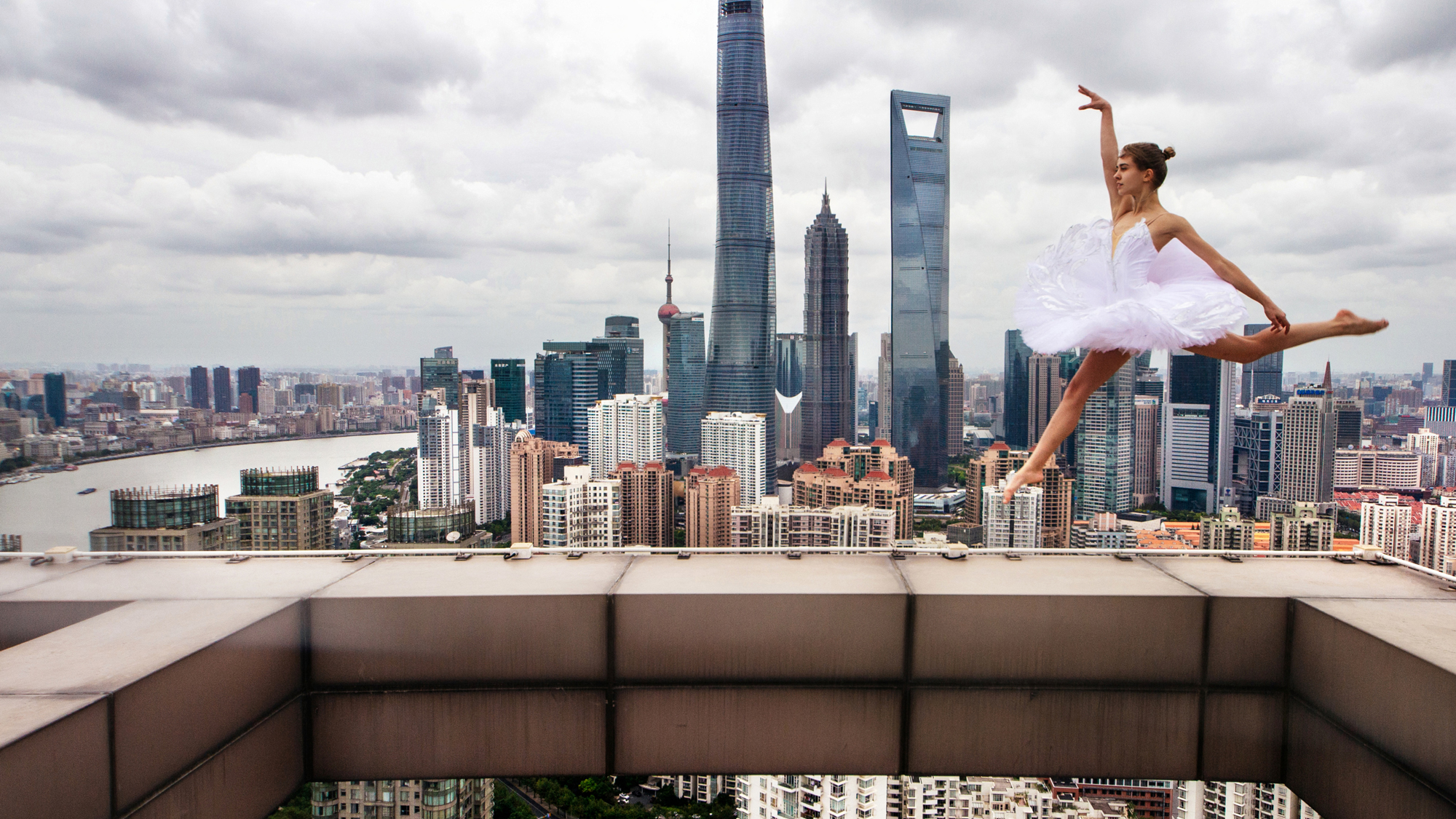 Woman in white tutu leaps on top of building with skyline in background
