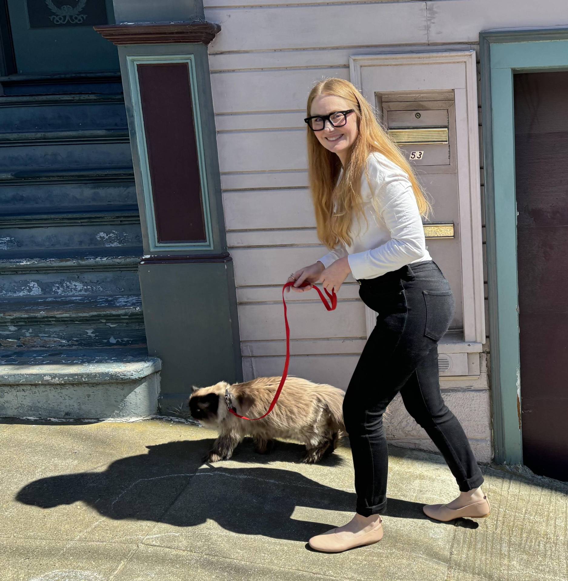 A smiling white woman with long blond hair walks a cat on a leash.