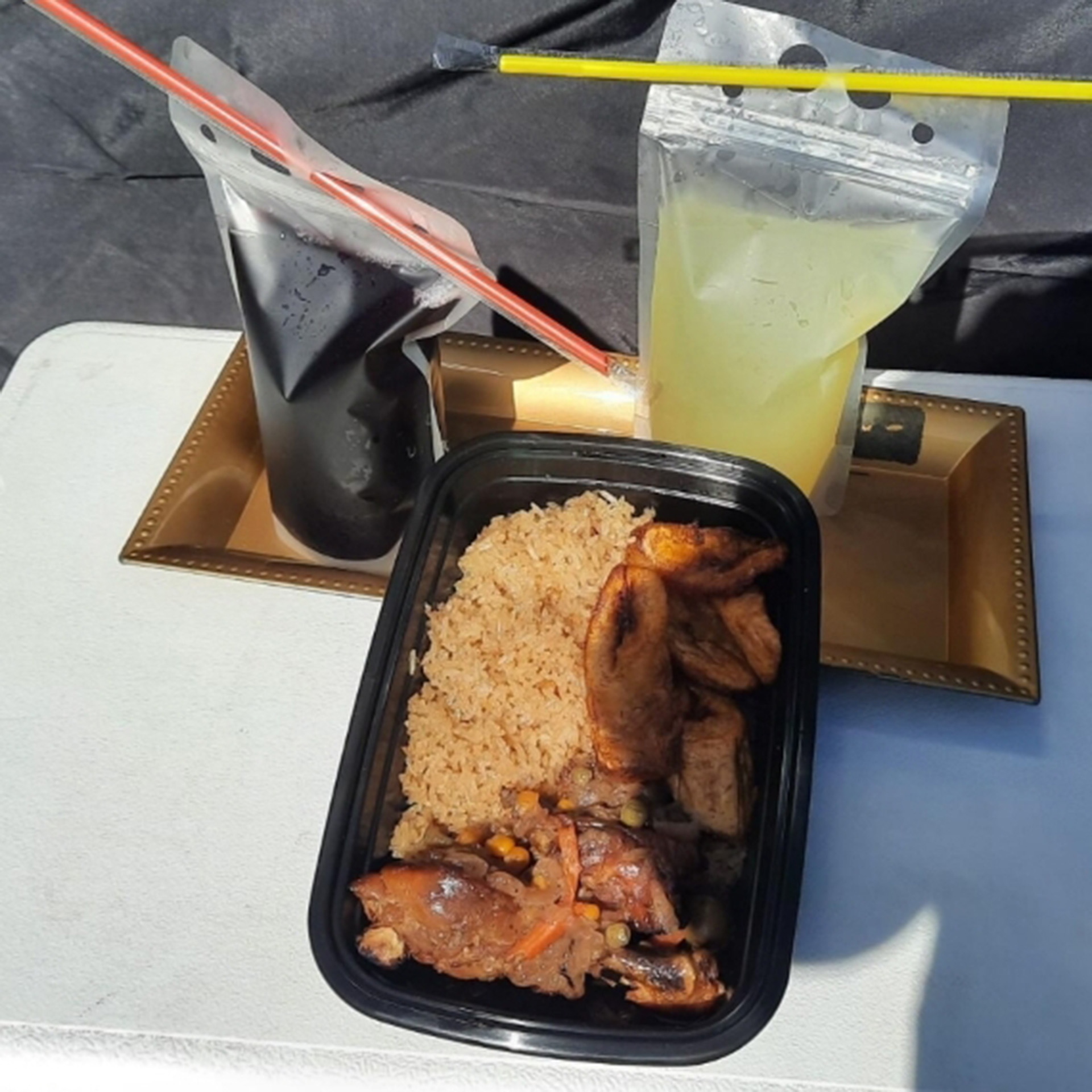 A takeout container of jollof rice and two plastic bags of juice.