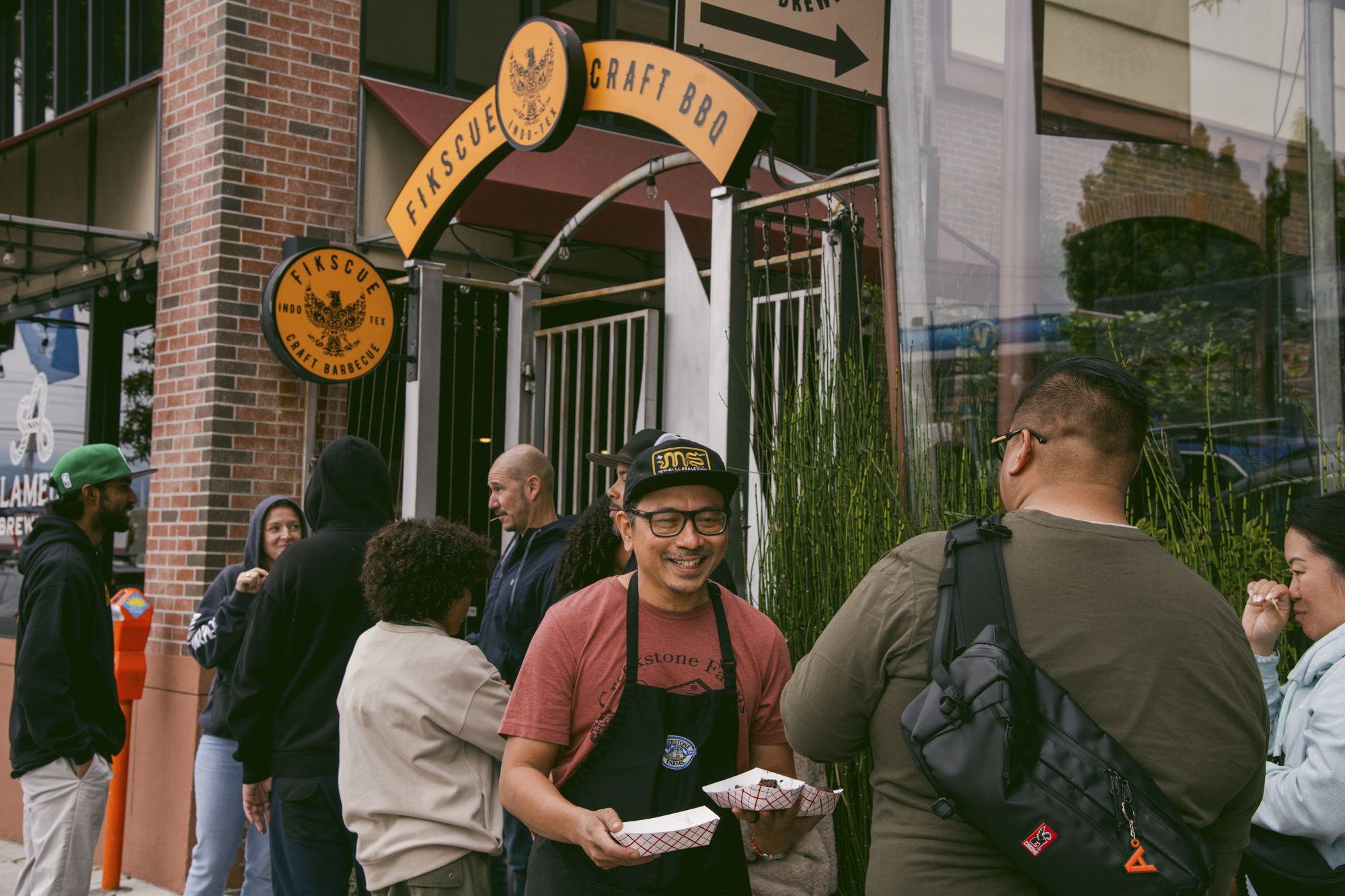 A barbecue chef in a black apron passes out samples to customers waiting in line.