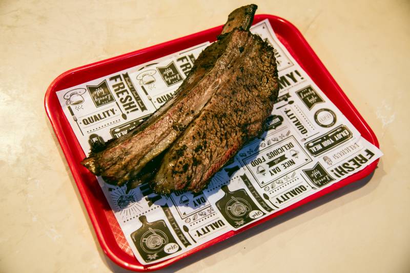 A huge smoked "dinosaur" beef rib on a paper-lined tray.