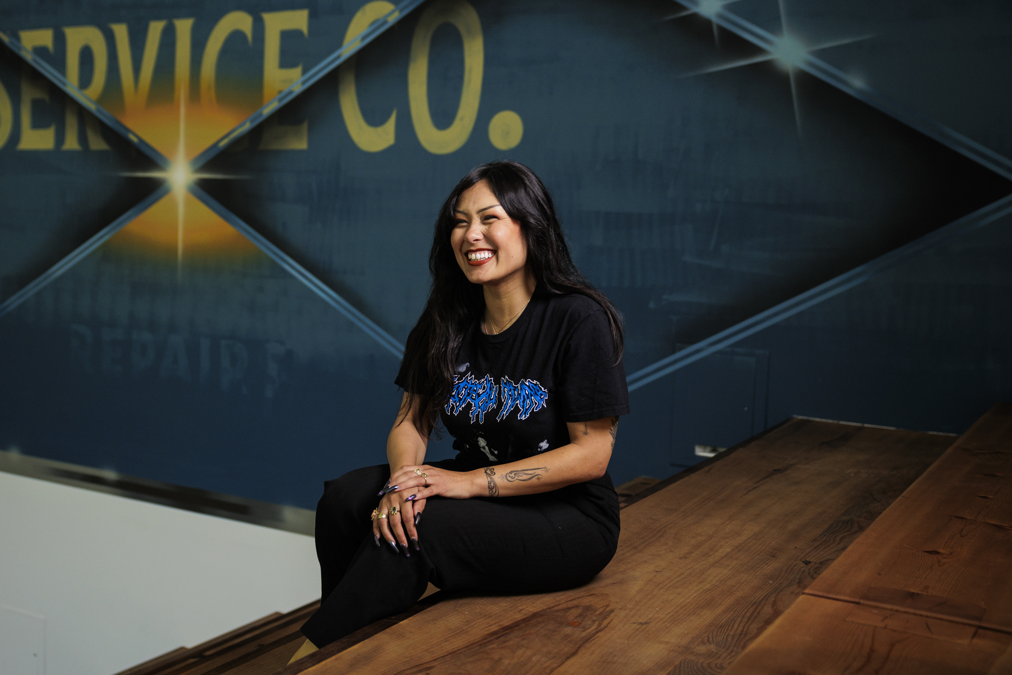 Person smiles sitting on wooden stairs with painted mural behind 