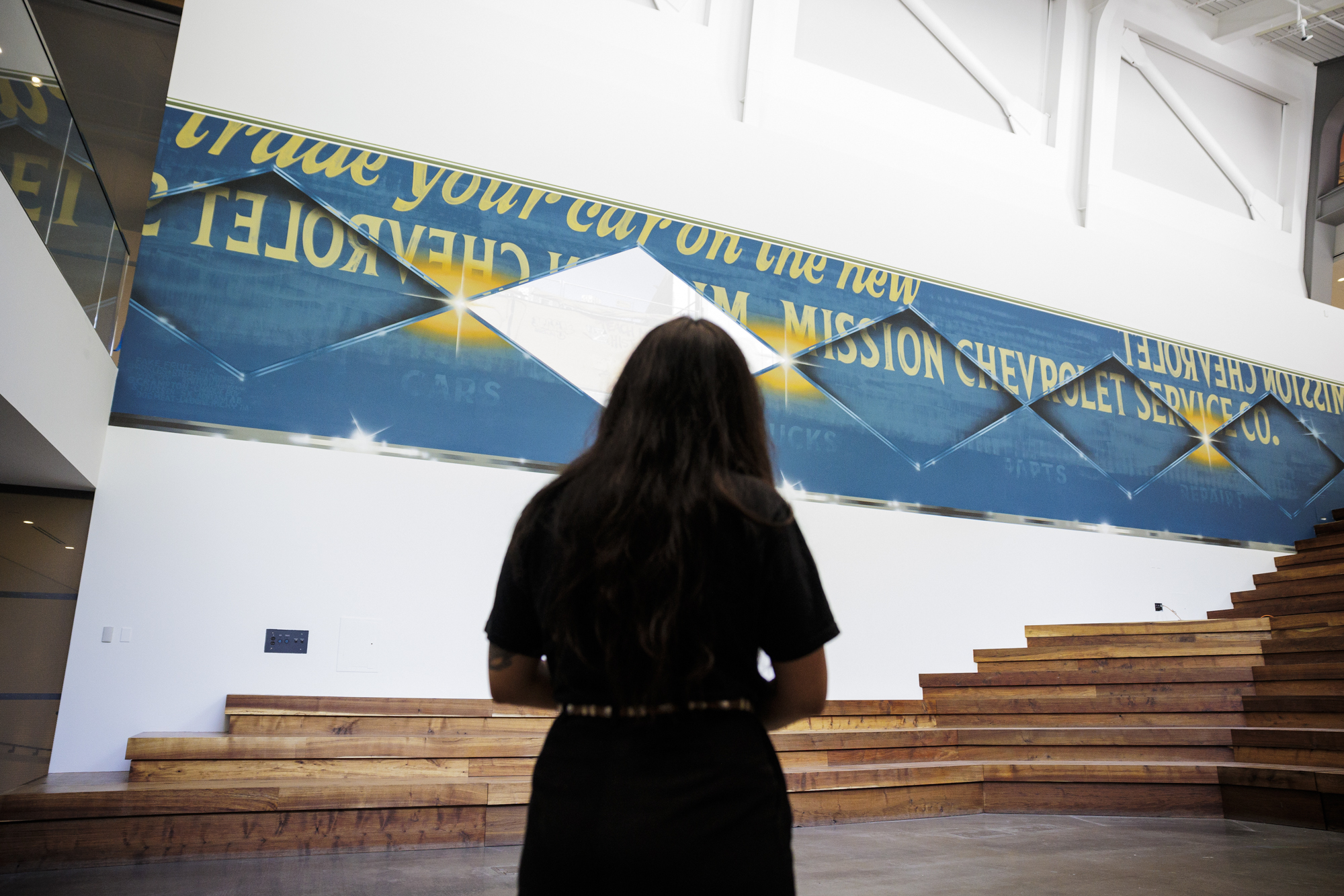 Person stands with back to camera looking up at large mural on wall