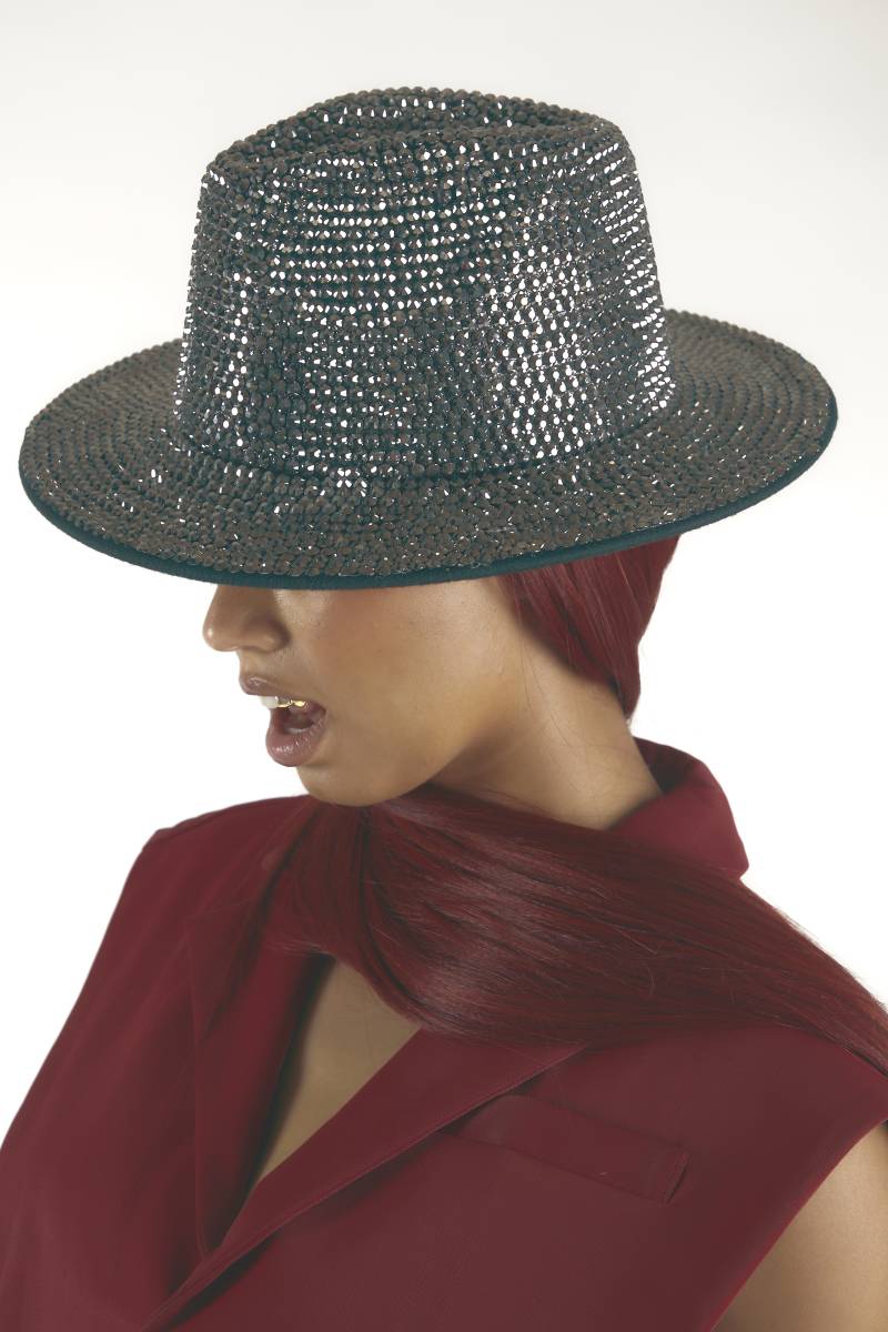 A woman in a bedazzled grey hat strikes a pose that allows you to see her gold teeth and dark red assemble.